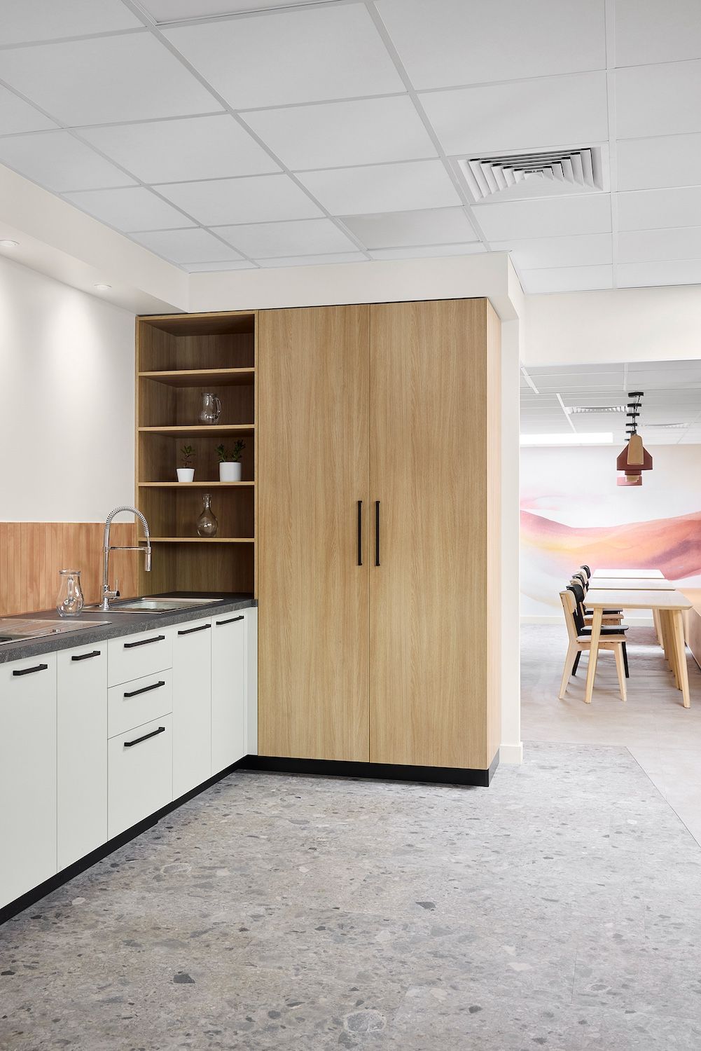 Coin repas de bureau avec placards blancs, rangements en bois et coin repas en arrière-plan