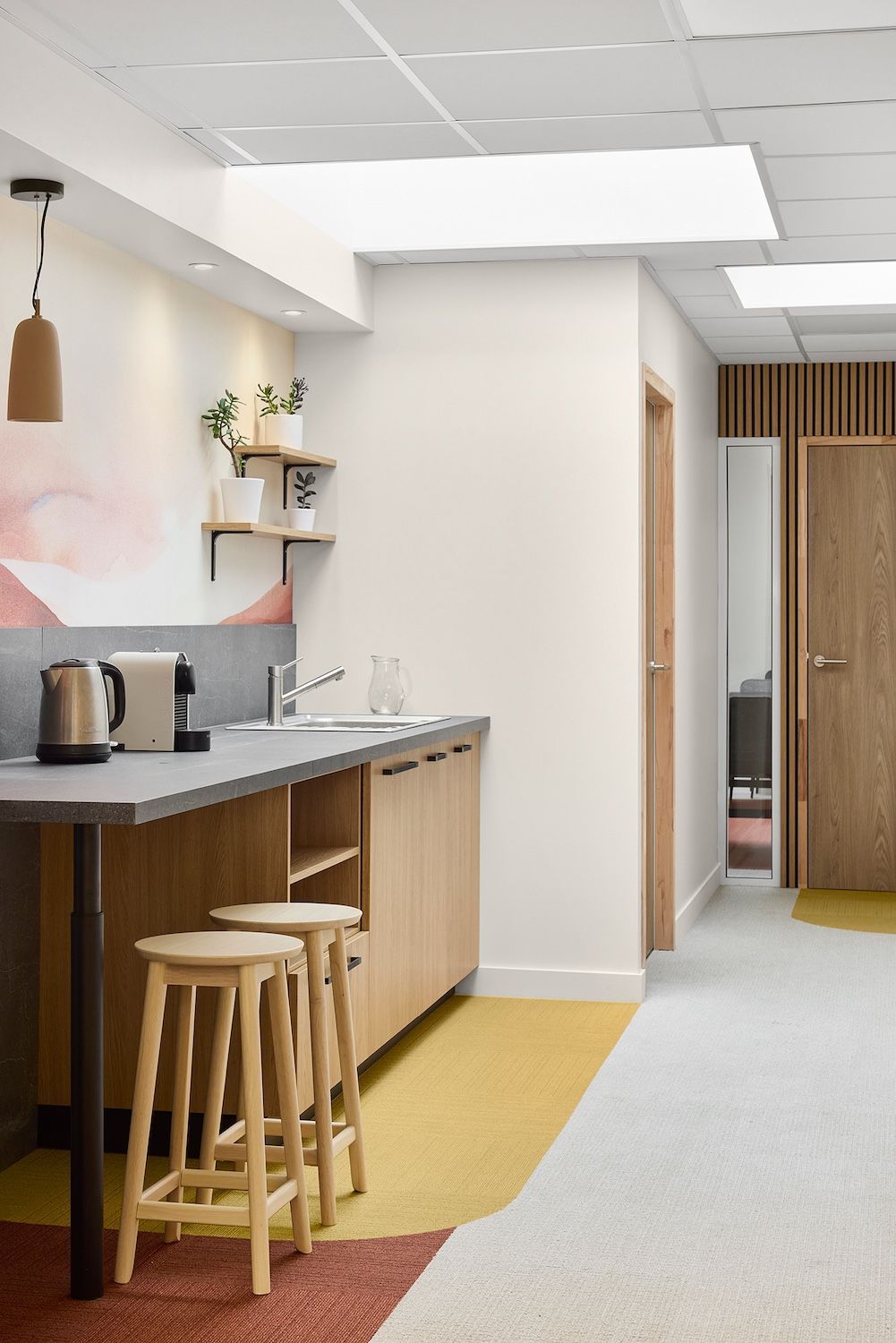Kitchenette moderne avec tabourets en bois, appareils électroménagers sur le plan de travail et un couloir dans une salle de pause lumineuse d'un bureau