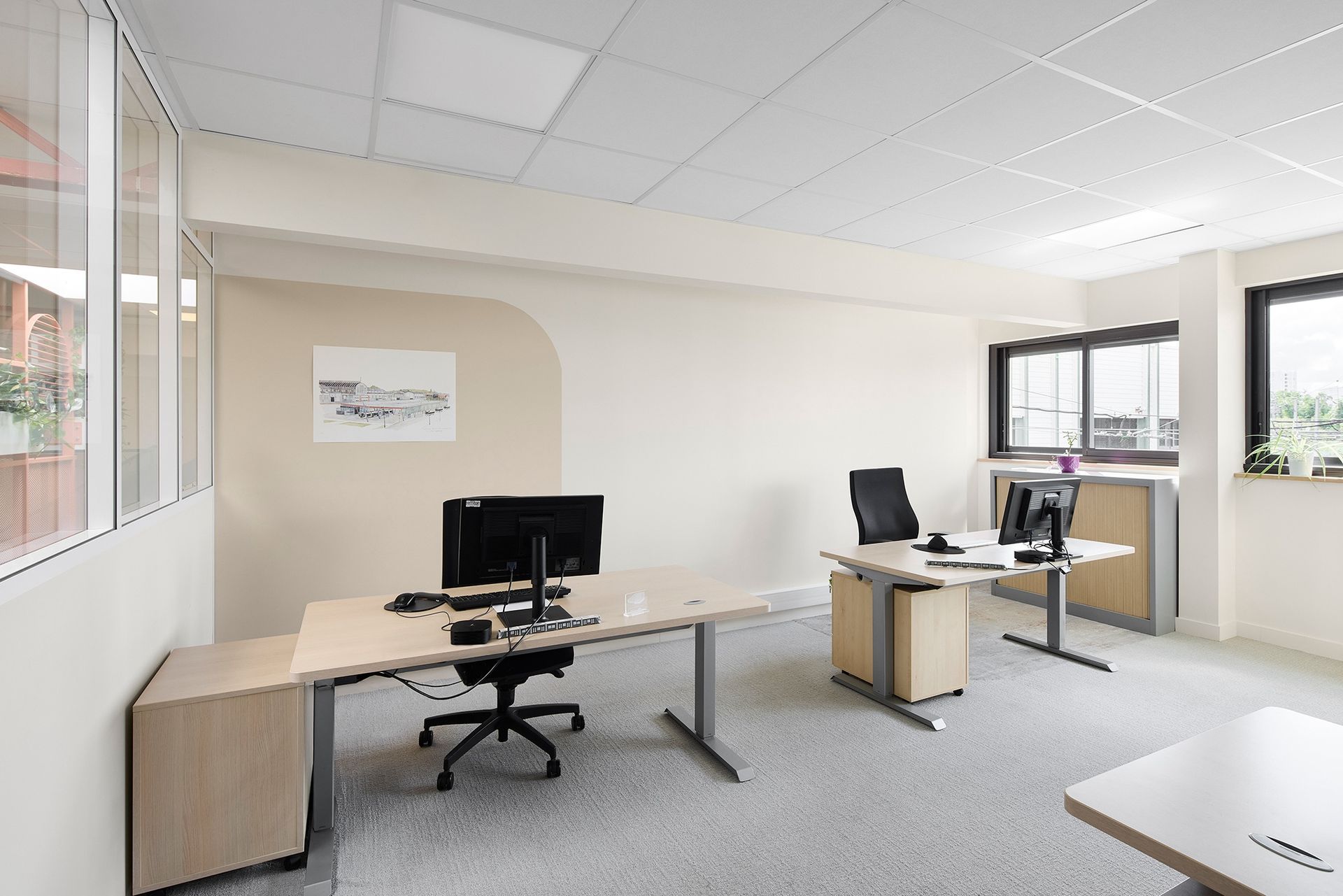 Bureau lumineux et vide, avec deux bureaux, des ordinateurs et de grandes fenêtres.