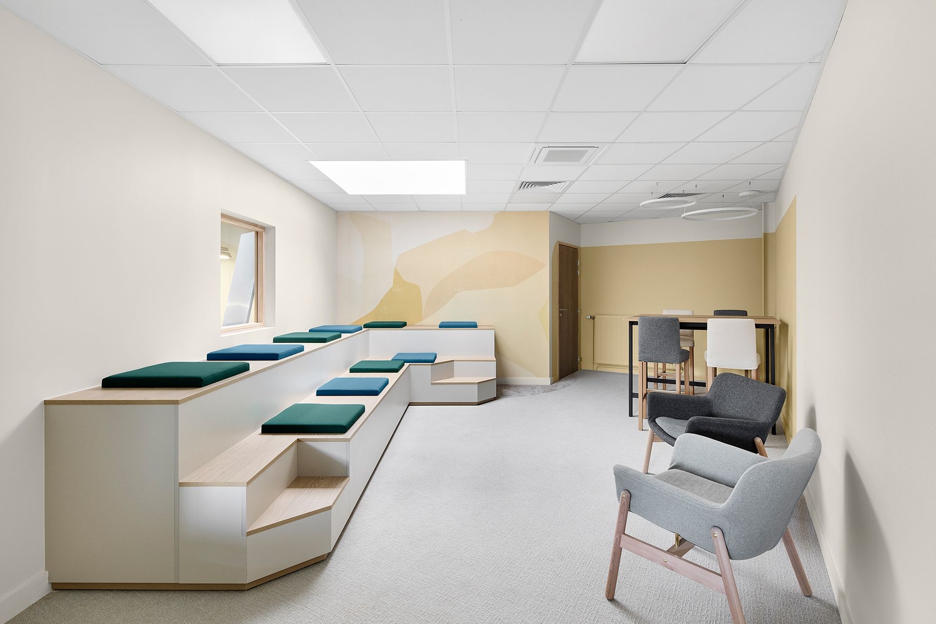 Salle d'attente vide d'une clinique avec des bancs vert menthe, des chaises grises et des plafonniers carrelés