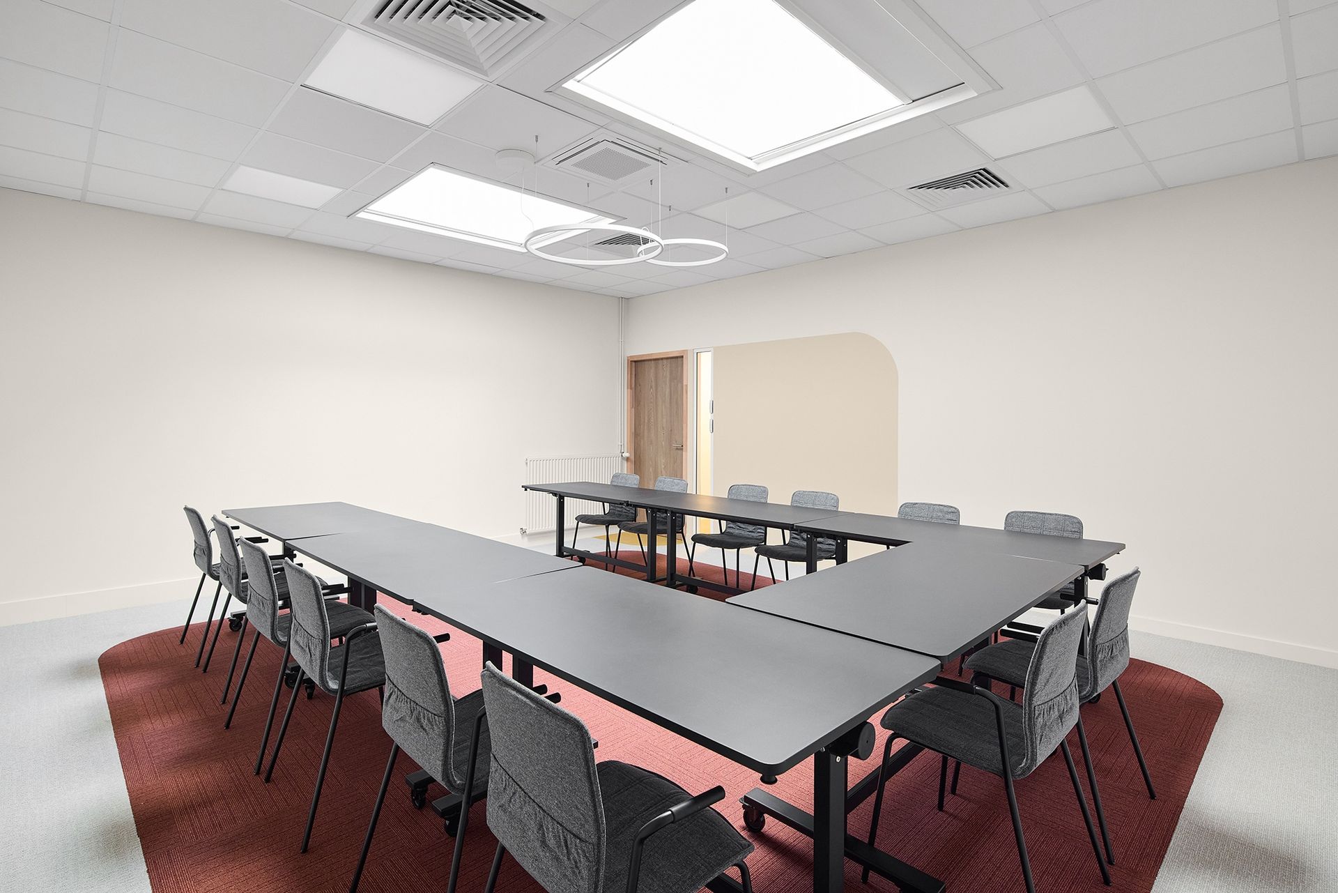 Salle de conférence moderne avec une table en forme de U, des chaises noires, une moquette rouge et des luminaires au plafond
