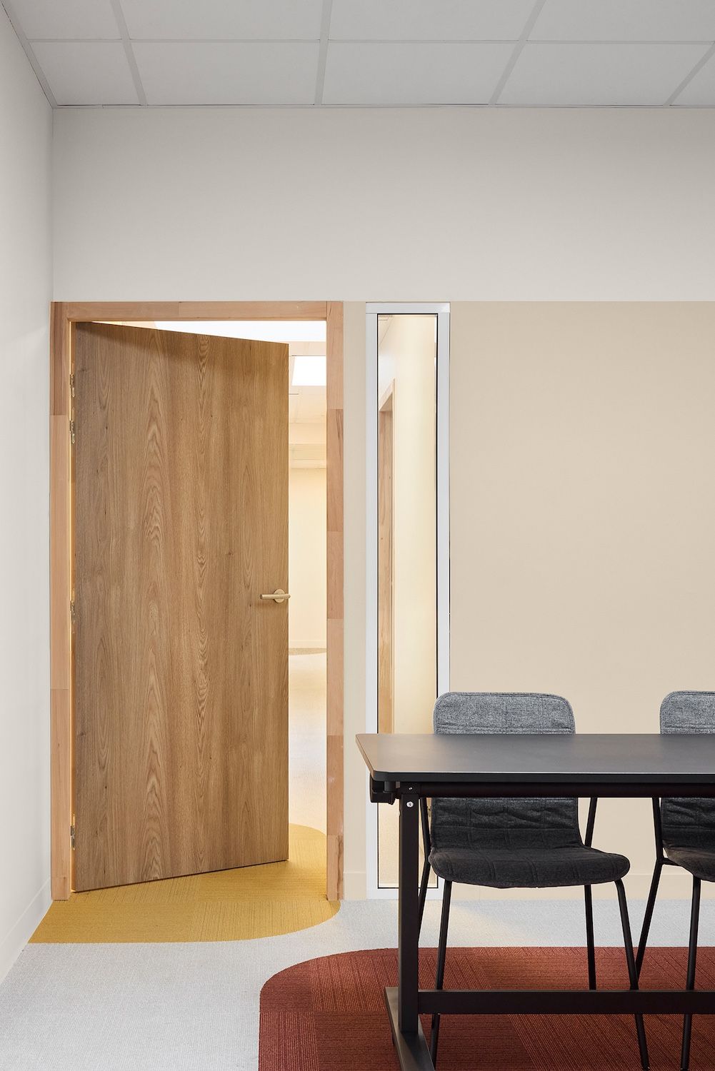 Petite salle de réunion avec porte en bois ouverte, table, chaise noire et tapis rouge.