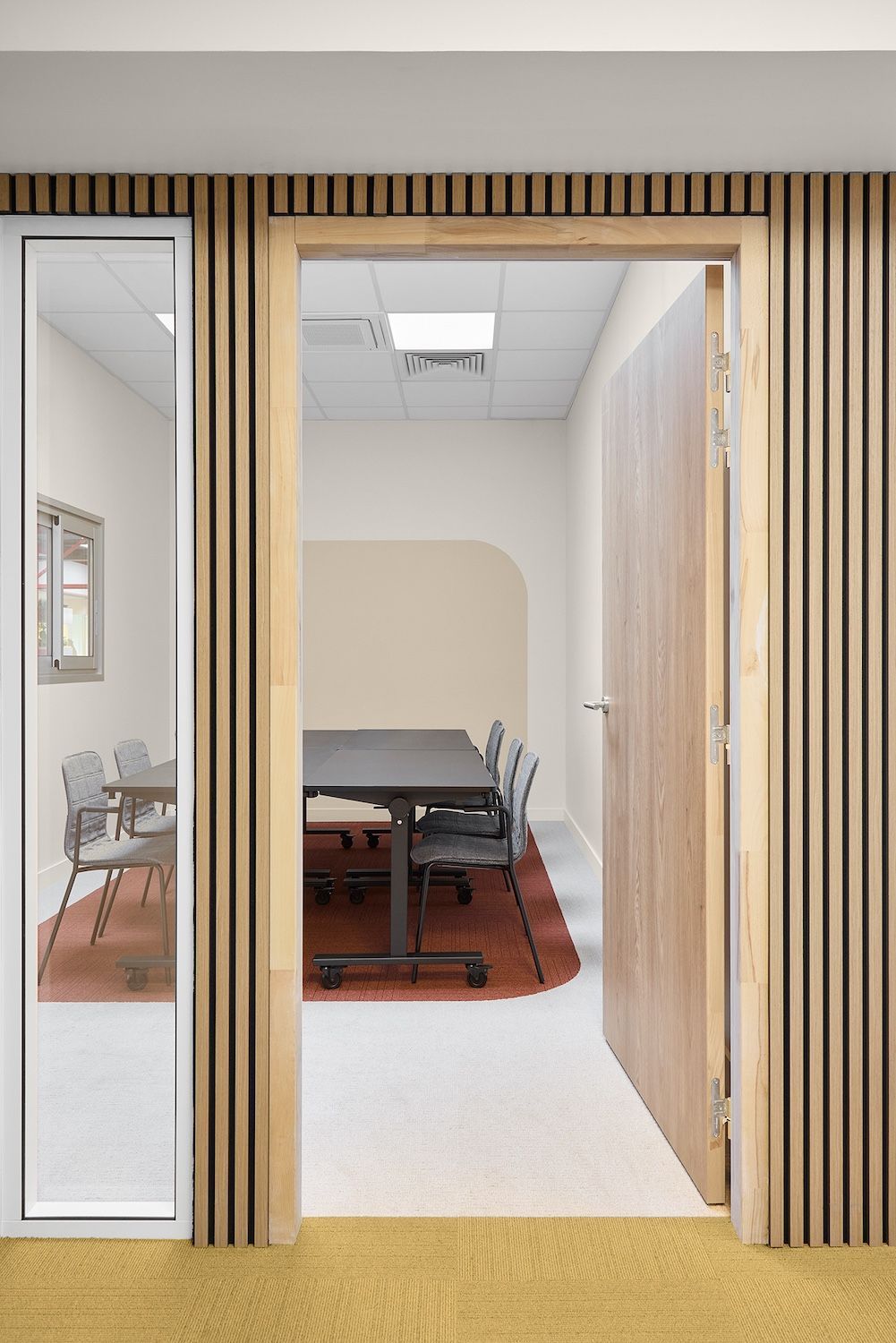 Porte de bureau moderne avec cloison à lattes de bois, panneau de verre et table de réunion à l'intérieur