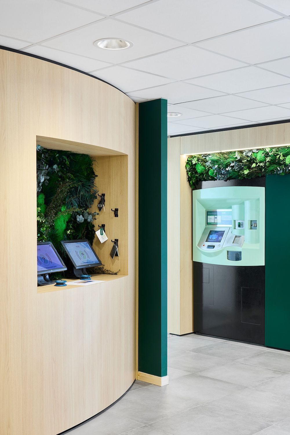 Kiosque à café moderne avec tabourets en bois, murs verts et suspensions lumineuses blanches dans un centre commercial