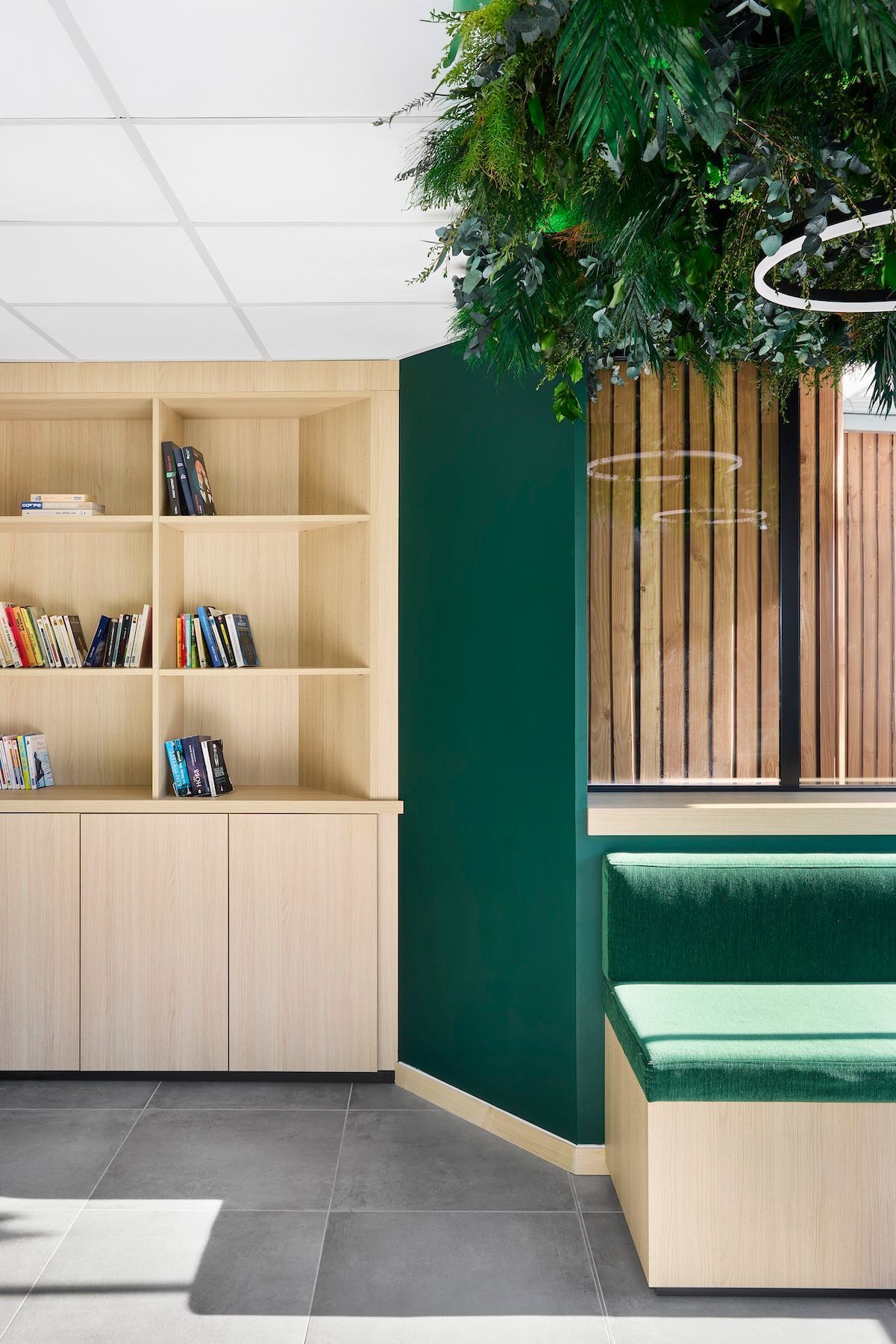 Coin bureau moderne avec bibliothèque en bois, mur végétal, banquette et grand arbre d'intérieur.