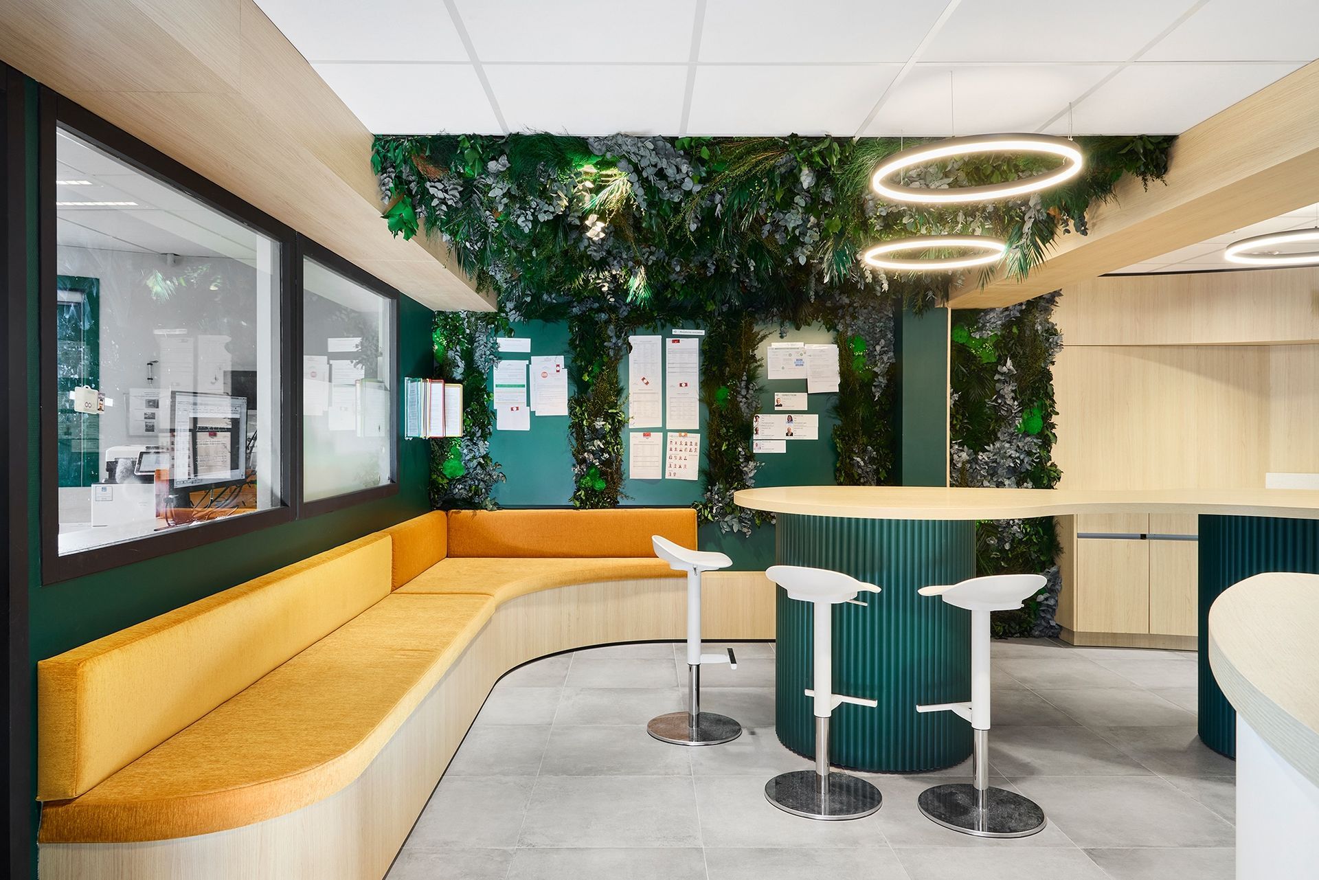 Espace d'accueil moderne avec bureaux blancs, éléments en bois et mur végétal près d'une fenêtre.