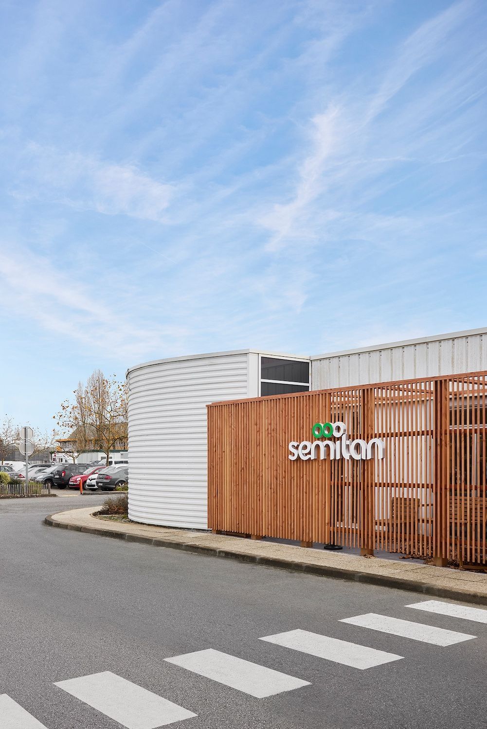 Porte vert foncé ornée d'une ligne et d'un cercle orange dans un couloir moderne, encadrée par des étagères en bois.