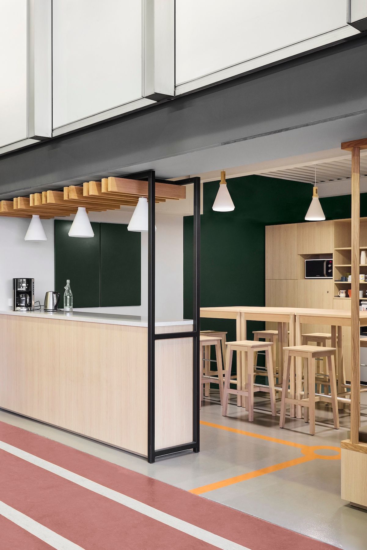 Kiosque à café moderne avec tabourets en bois, murs verts et suspensions lumineuses blanches dans un centre commercial