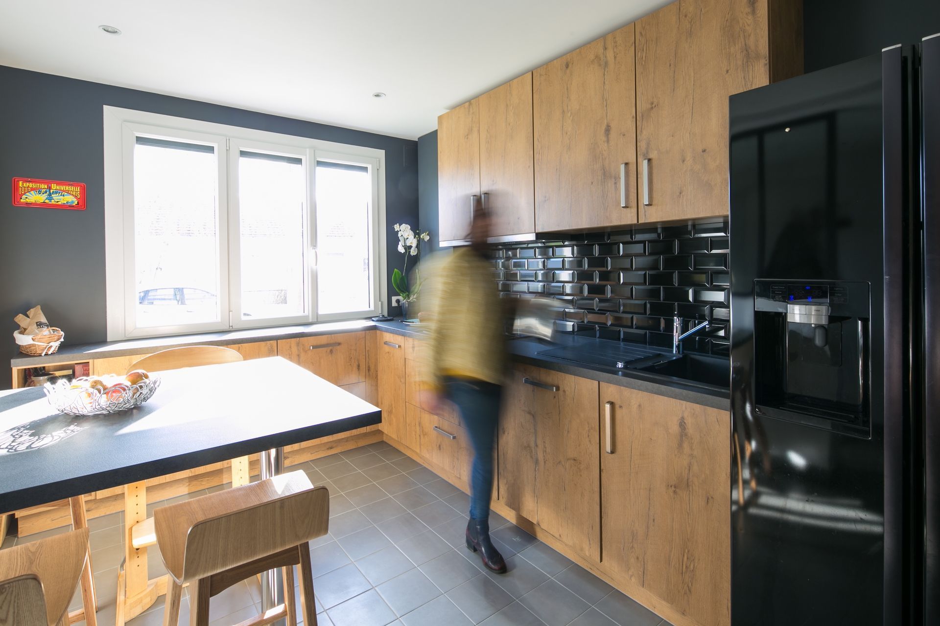 Cuisine moderne avec placards en bois, électroménager noir et une personne debout près du comptoir