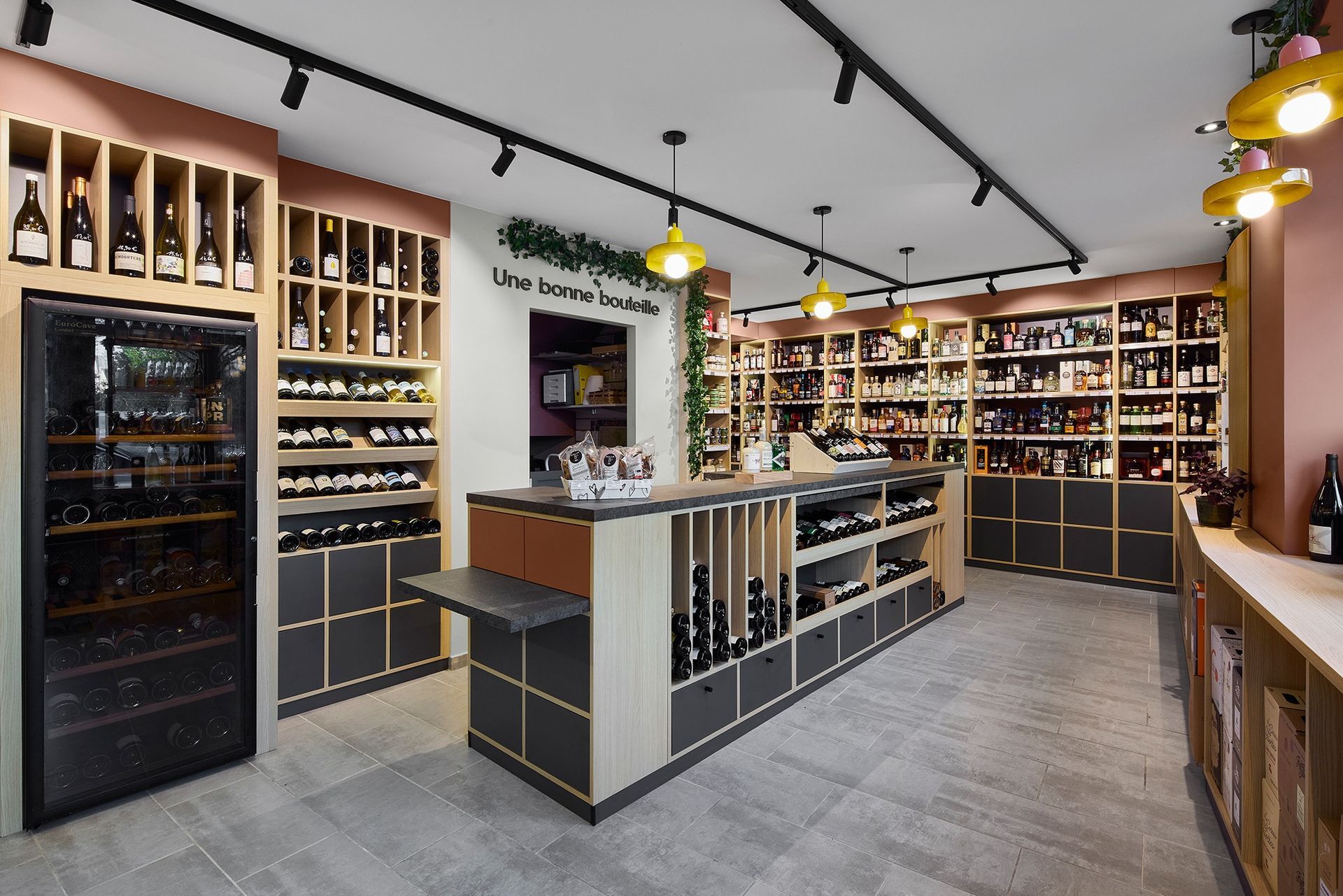 Intérieur moderne d'une cave à vin avec des étagères de bouteilles, un îlot central et un éclairage suspendu chaleureux.