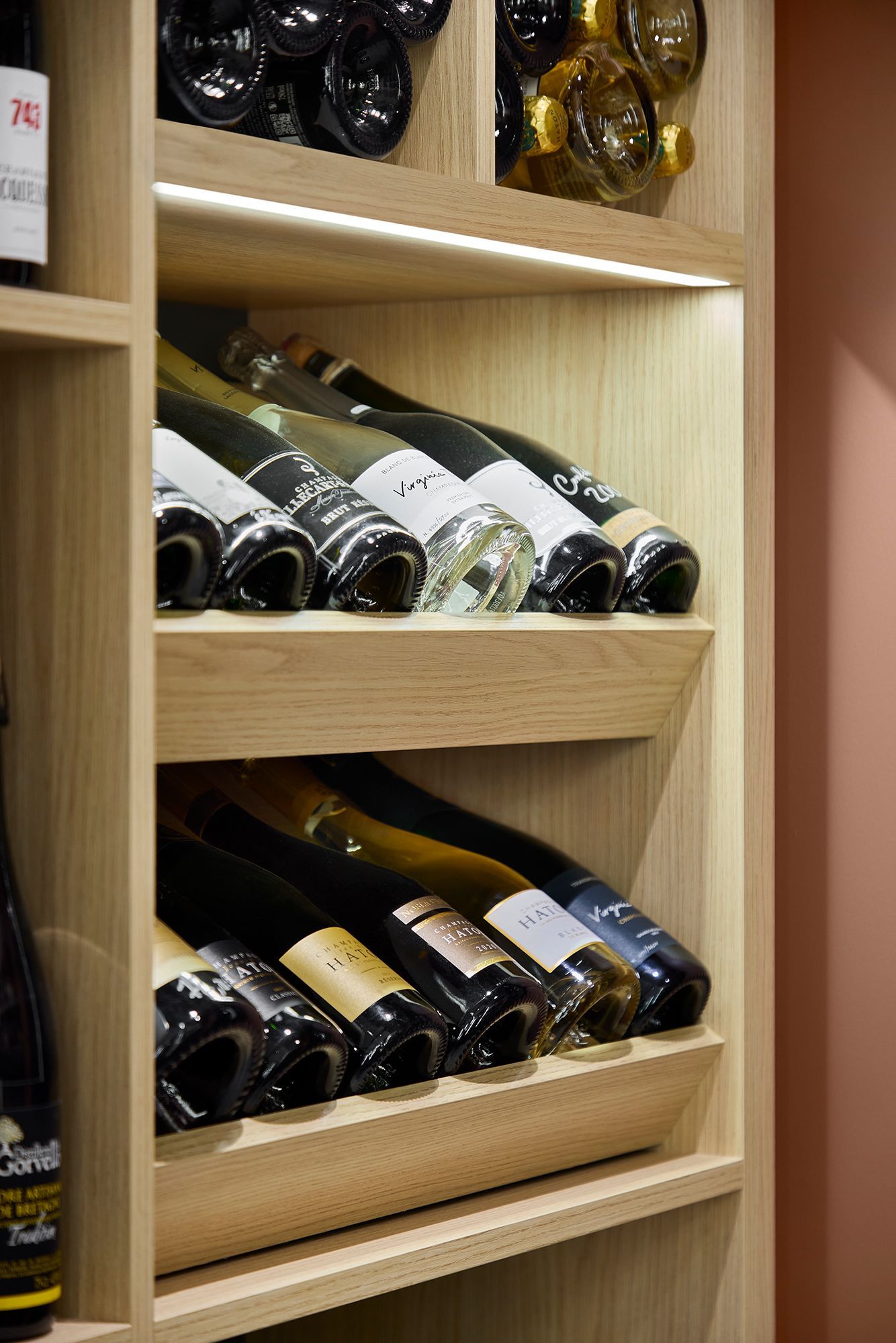 Un casier à vin en bois rempli de bouteilles de vin assorties, principalement en verre foncé, dans une vitrine de magasin.