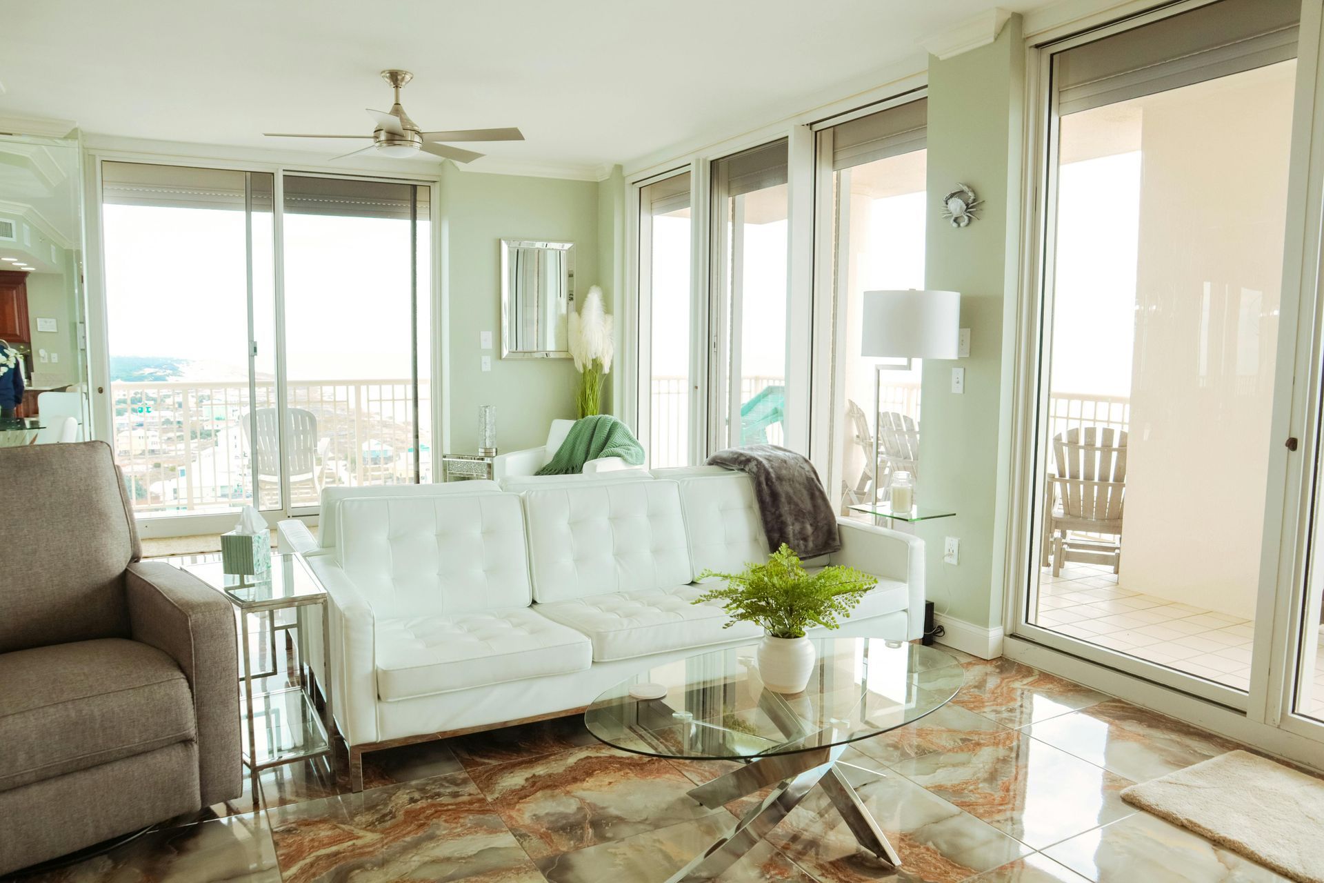 Salon lumineux avec canapé blanc, table basse en verre, grandes fenêtres et vue sur le balcon