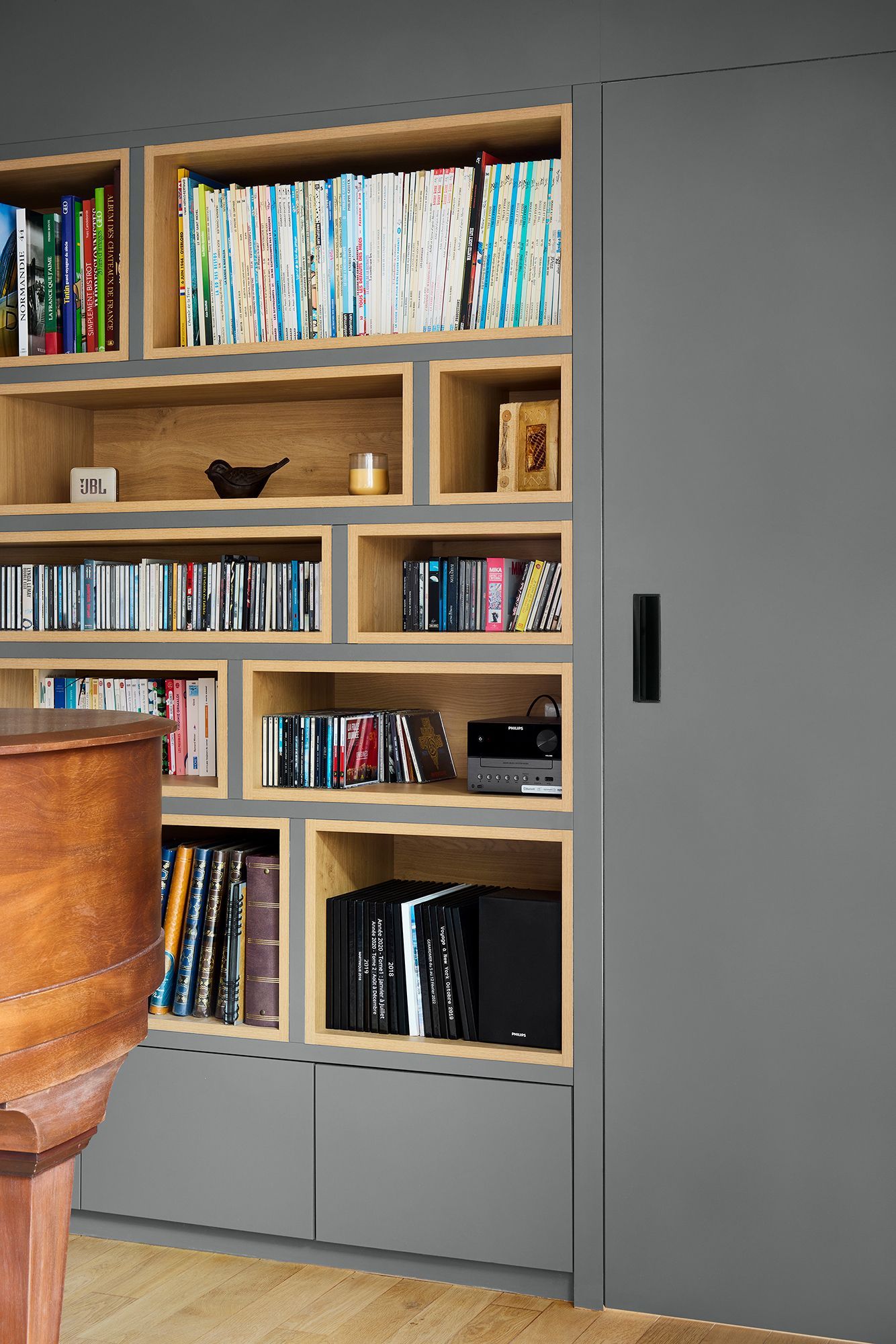 Bibliothèque encastrée en bois avec livres et objets de décoration à côté d'une porte coulissante grise