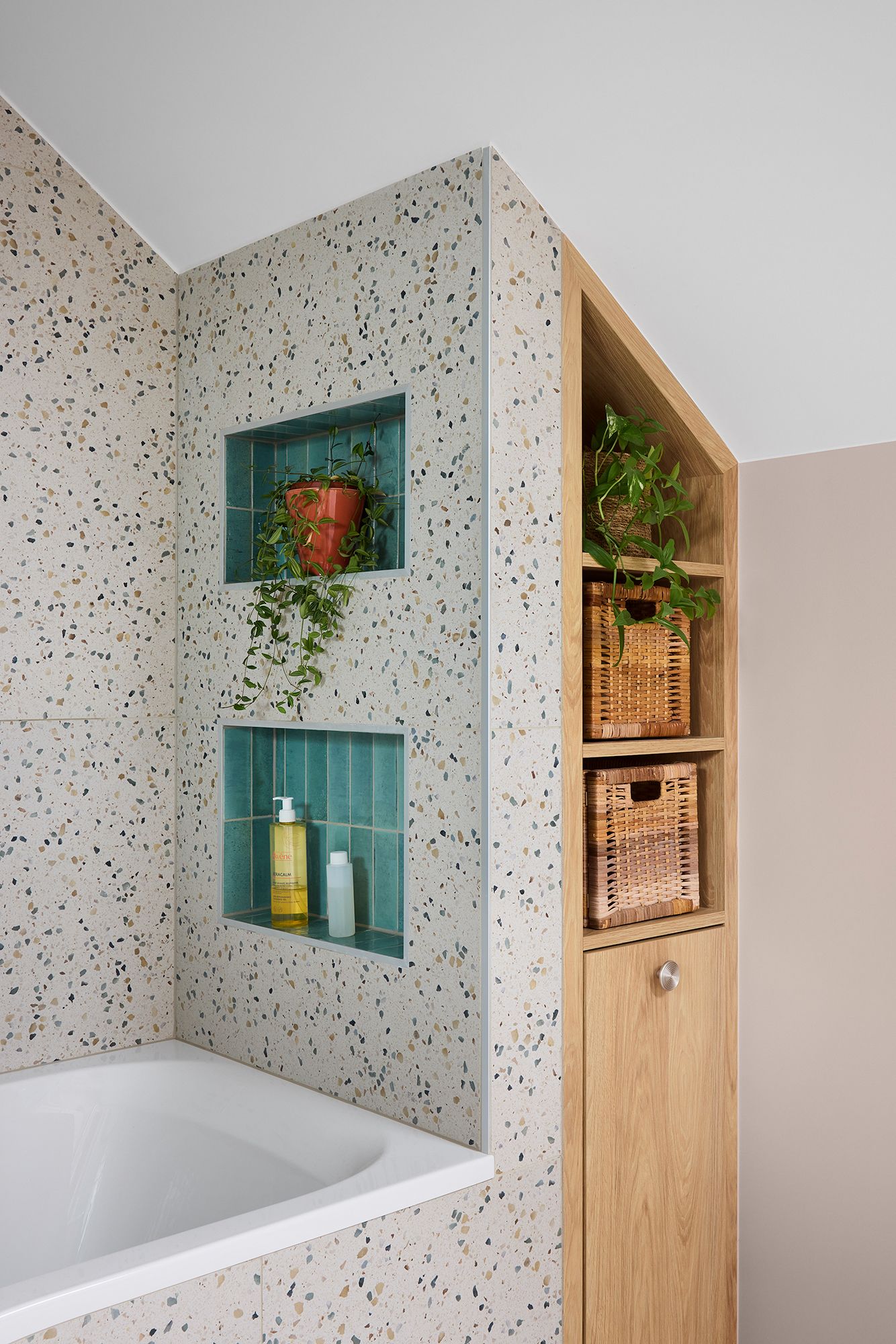 Coin salle de bain moderne avec carrelage moucheté, étagères encastrées, baignoire et meuble de rangement en bois avec plantes.