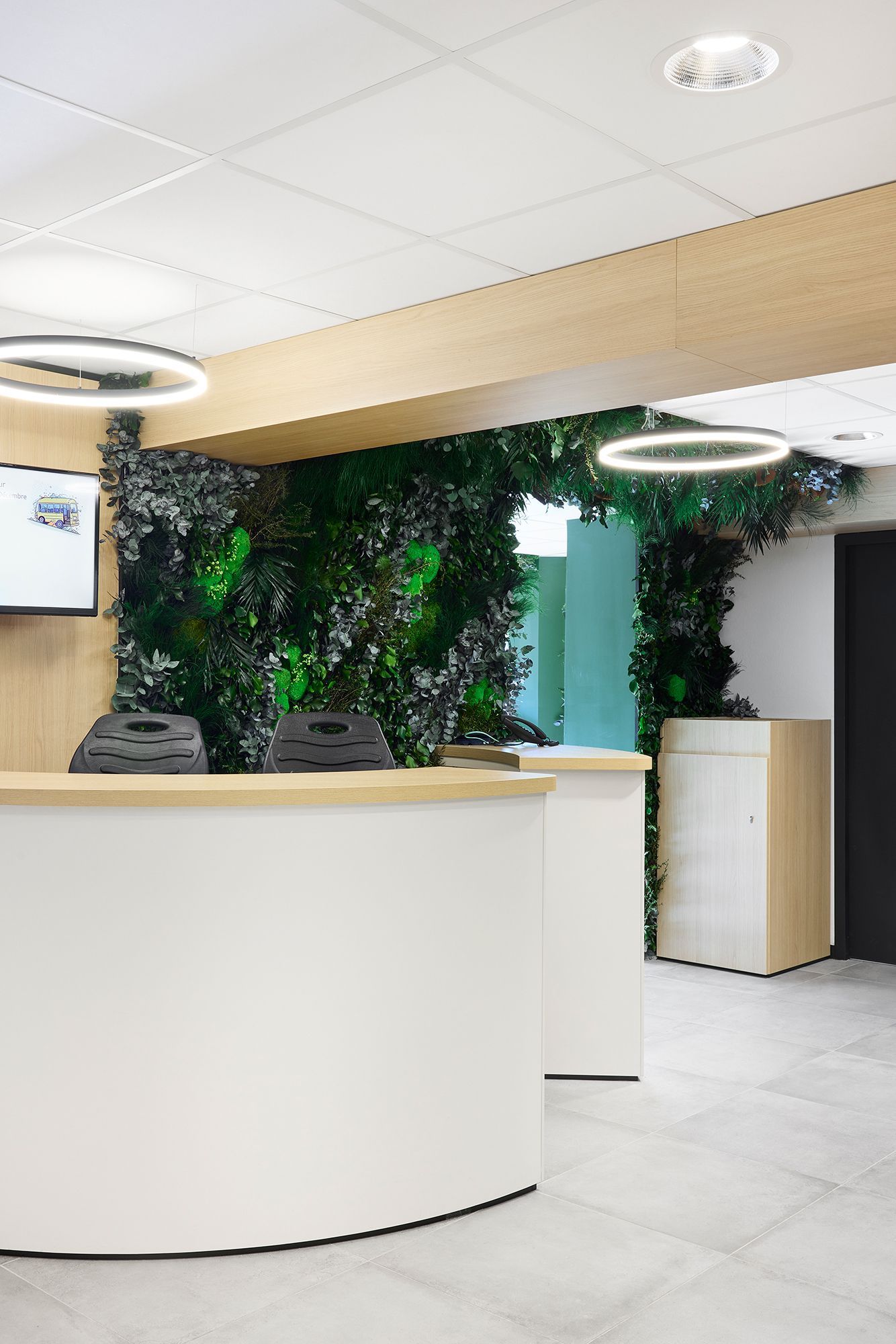 Espace d'accueil moderne avec bureau blanc, mur végétal et luminaires suspendus circulaires