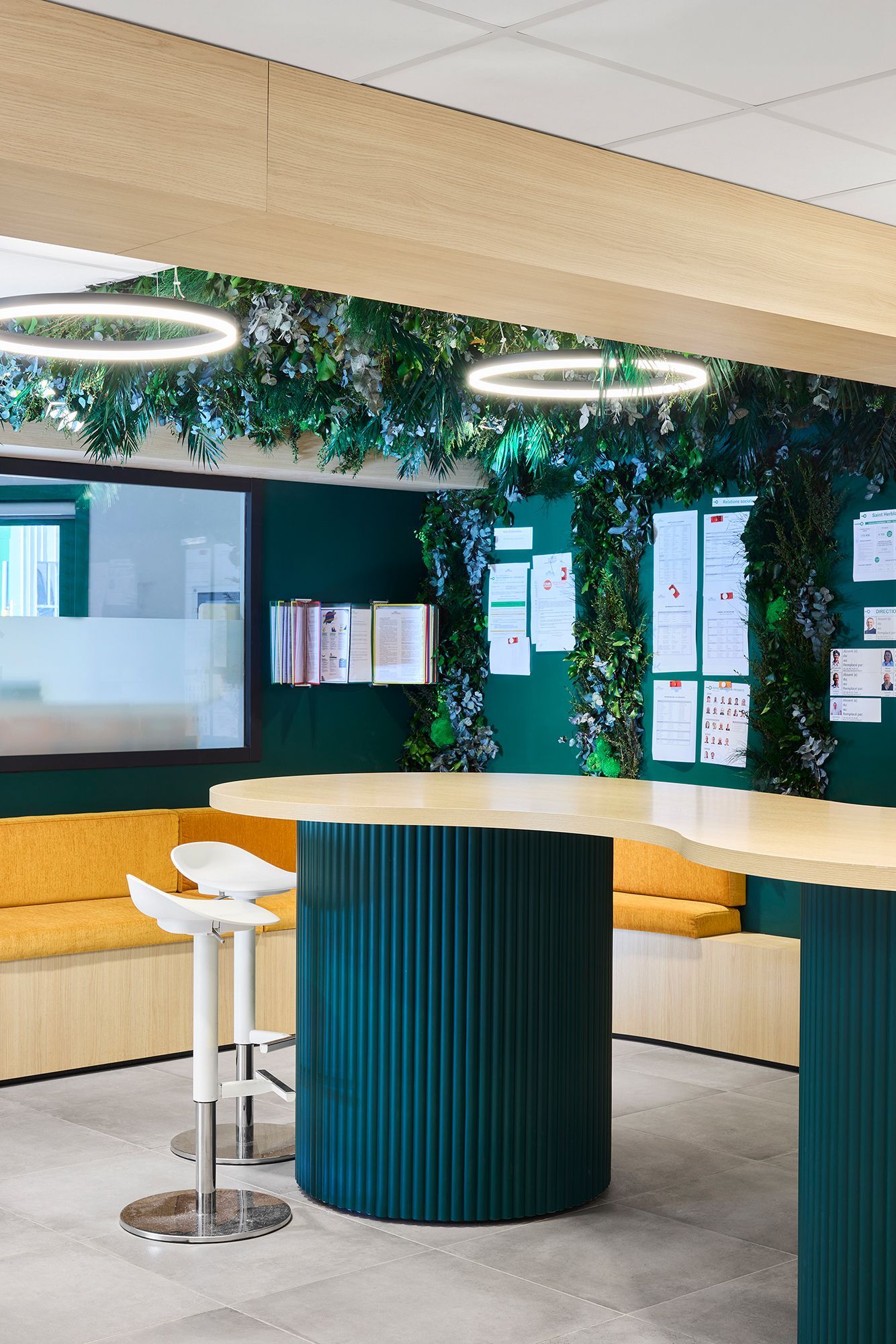 Salon moderne avec mur végétal, luminaires circulaires au plafond, banquette jaune et table ronde turquoise