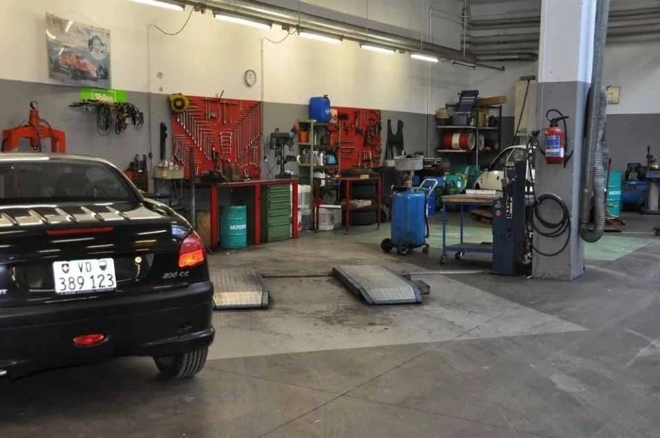 Voiture noire dans un garage avec outils, ponts élévateurs et équipements en arrière-plan
