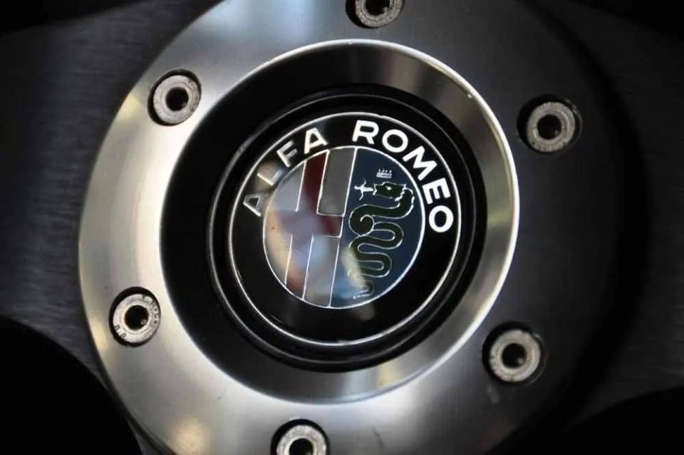 Gros plan sur un cache-moyeu de roue de voiture Alfa Romeo avec boulons argentés et jante noire.