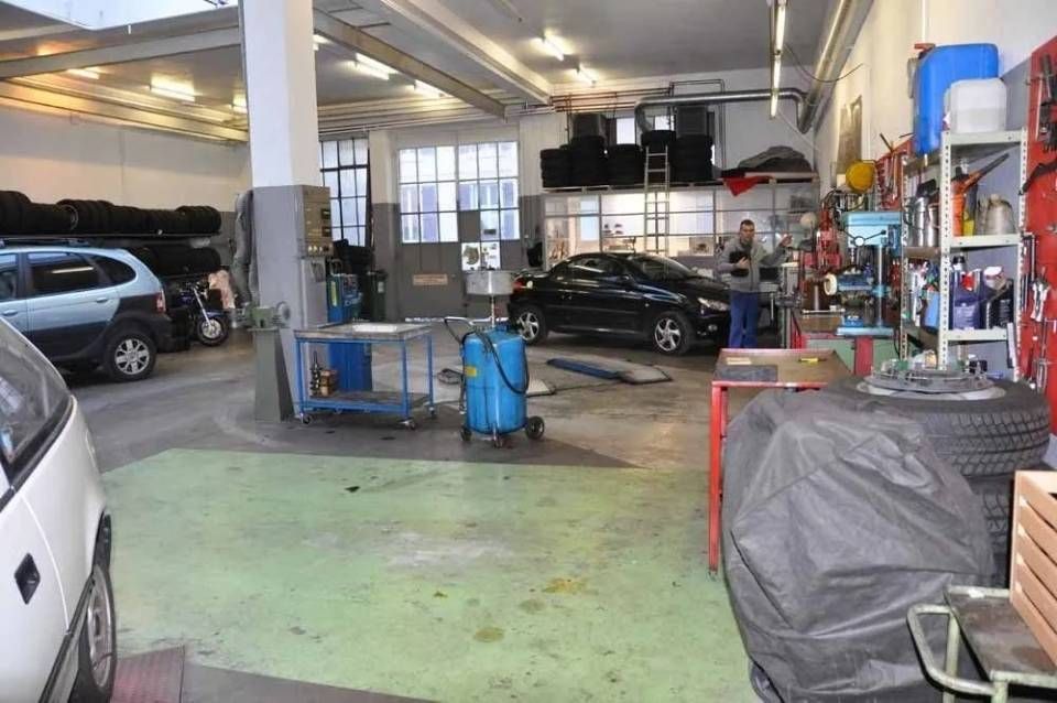 Intérieur d'un atelier de réparation automobile avec des voitures, des outils et du matériel dans un garage encombré.