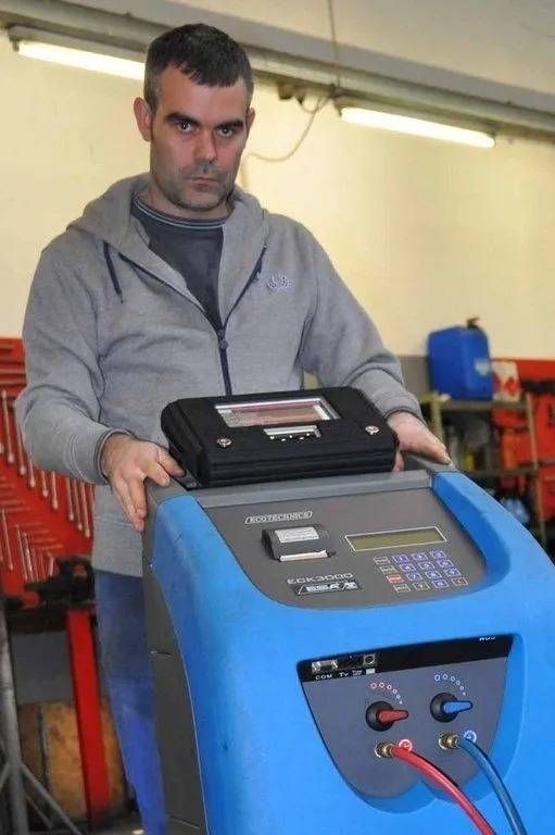Un homme se tient debout à côté d'une machine industrielle bleue sur laquelle est posé un ordinateur portable, dans un atelier.