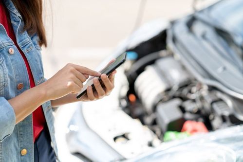 Frau tippt auf einem Handy, im Hintergrund ist der Vorderteil eines Autos mit offener Motorhaube
