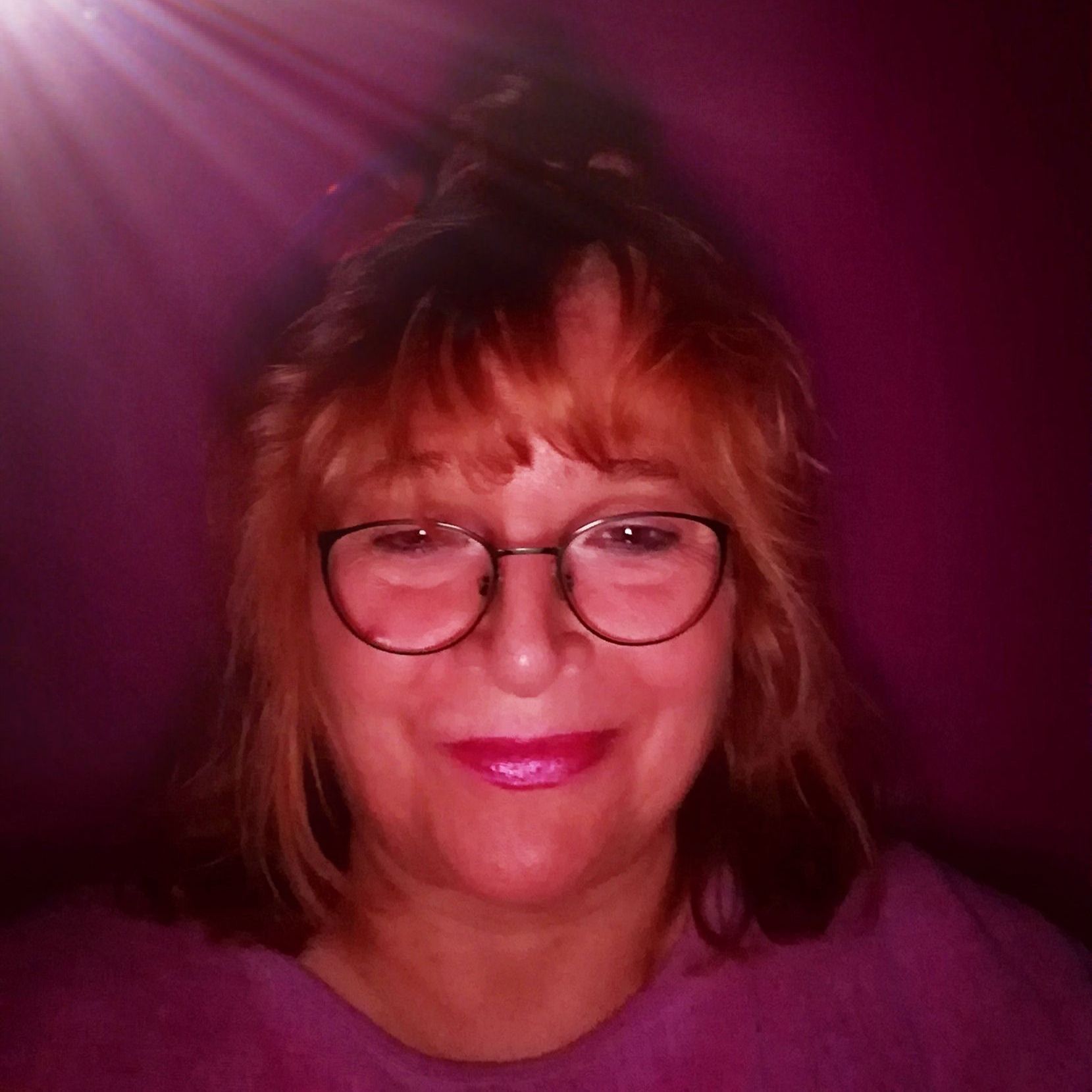 Eine Frau mit Brille und lila Hemd lächelt.