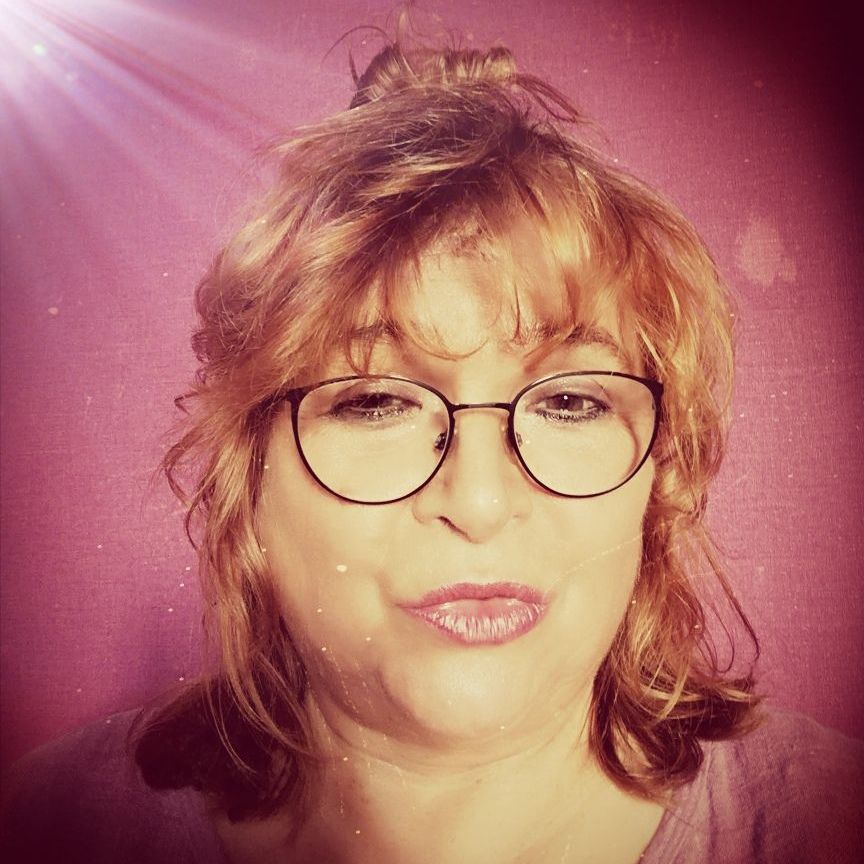 Eine Frau mit roten Haaren und Brille lächelt in die Kamera