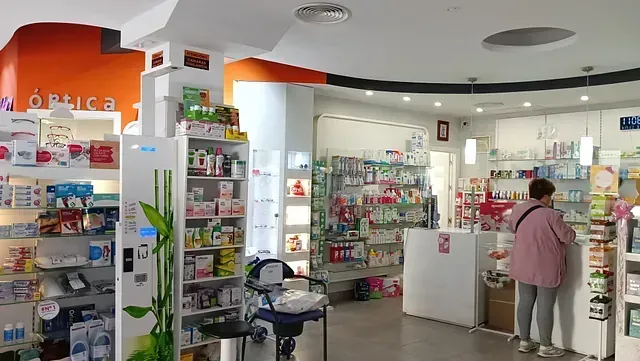 Interior de una farmacia con estantes de productos, un cliente en el mostrador y detalles en color naranja.