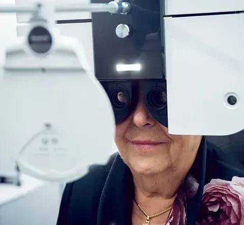 Mujer sometiéndose a un examen ocular, mirando a través de una máquina con los ojos enfocados en una clínica.