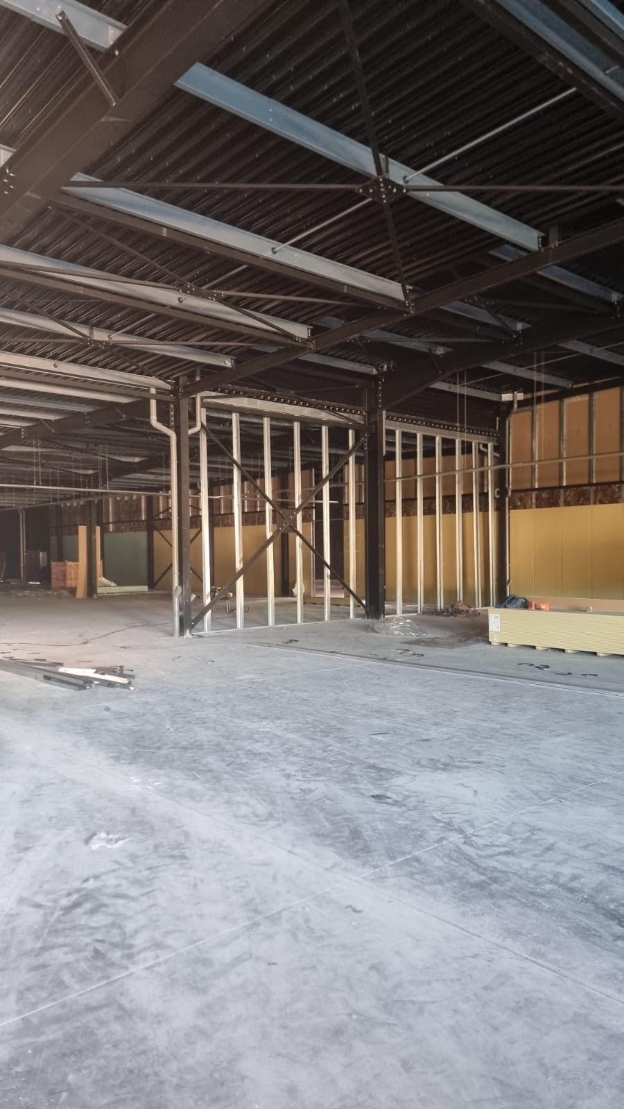 Intérieur d'entrepôt vide avec poutres apparentes au plafond, montants de charpente et sol en béton en construction.