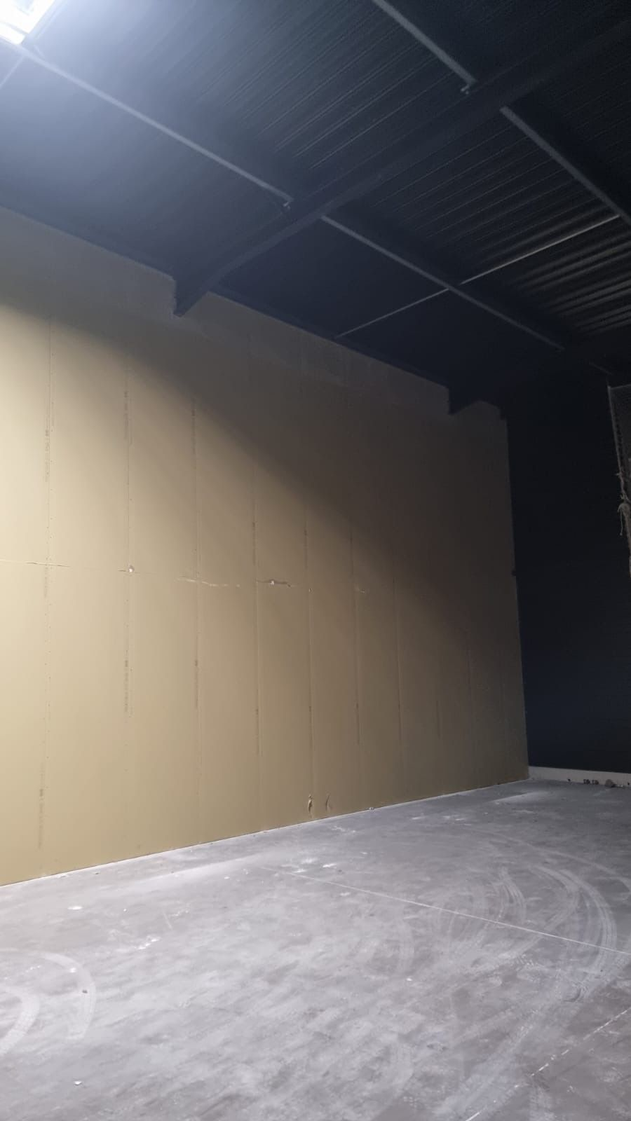 Entrepôt intérieur vide avec un mur beige, un plafond sombre et un sol en béton.