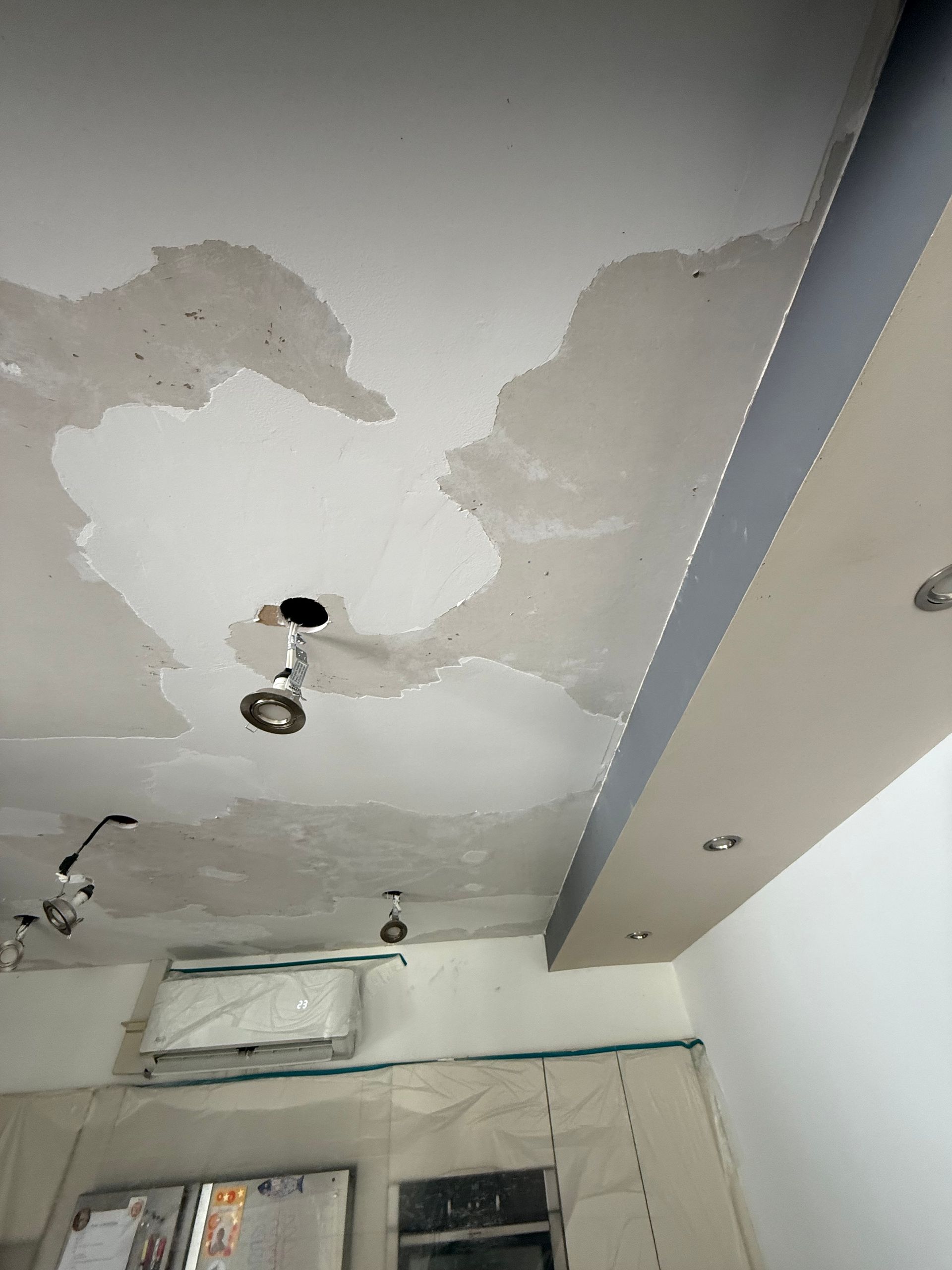 Peinture du plafond qui s'écaille et dégâts d'eau au-dessus d'une pièce avec des luminaires apparents.