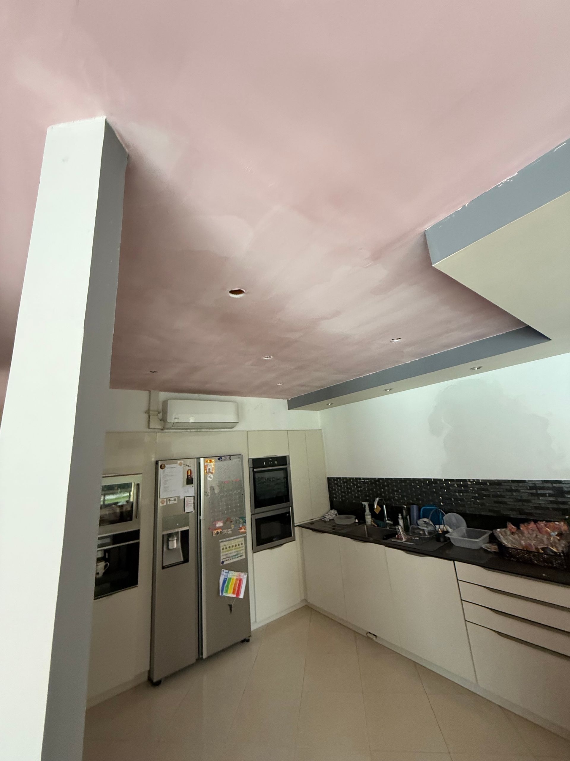 Cuisine avec armoires blanches, réfrigérateur en acier inoxydable, comptoirs en granit et plafond rose.