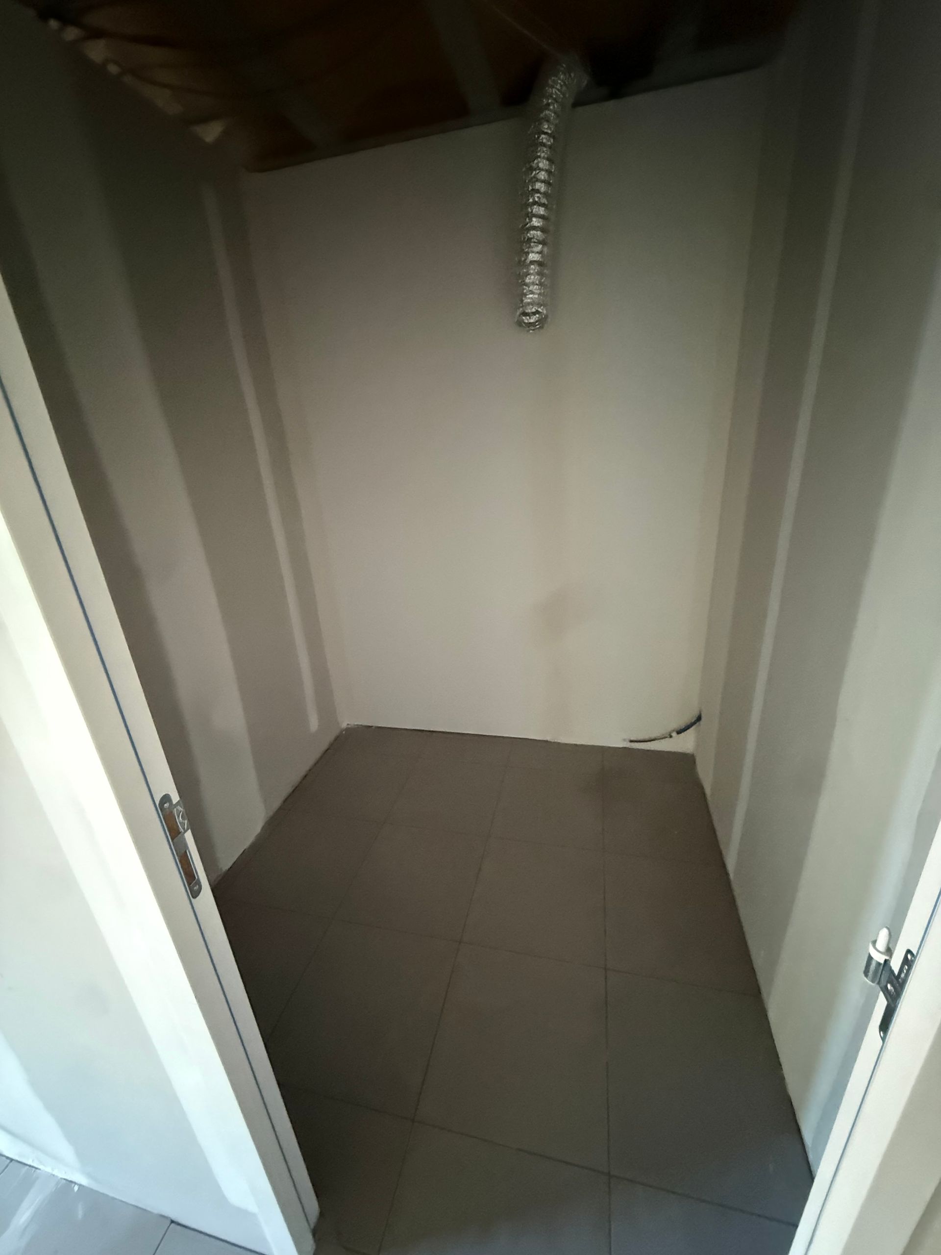 Dressing vide avec murs blancs, sol carrelé gris et une chaîne suspendue au plafond.