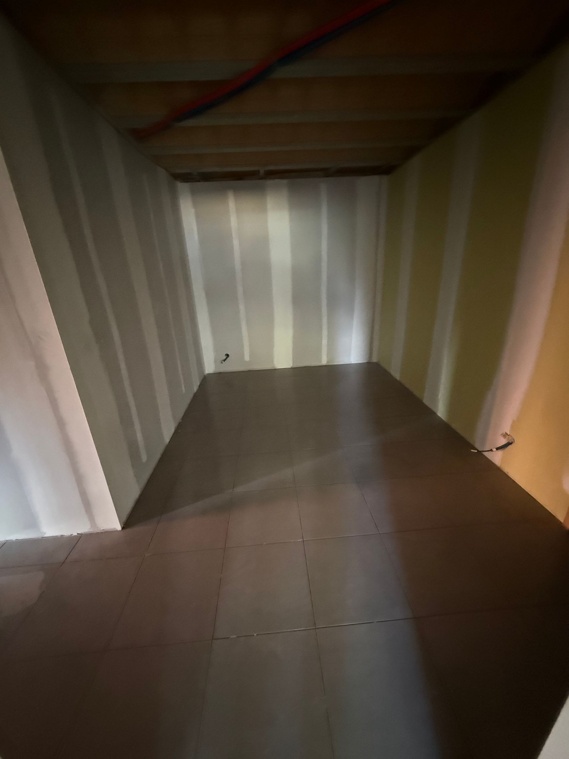 Débarras vide avec murs rayés, plafond bas et sol carrelé.