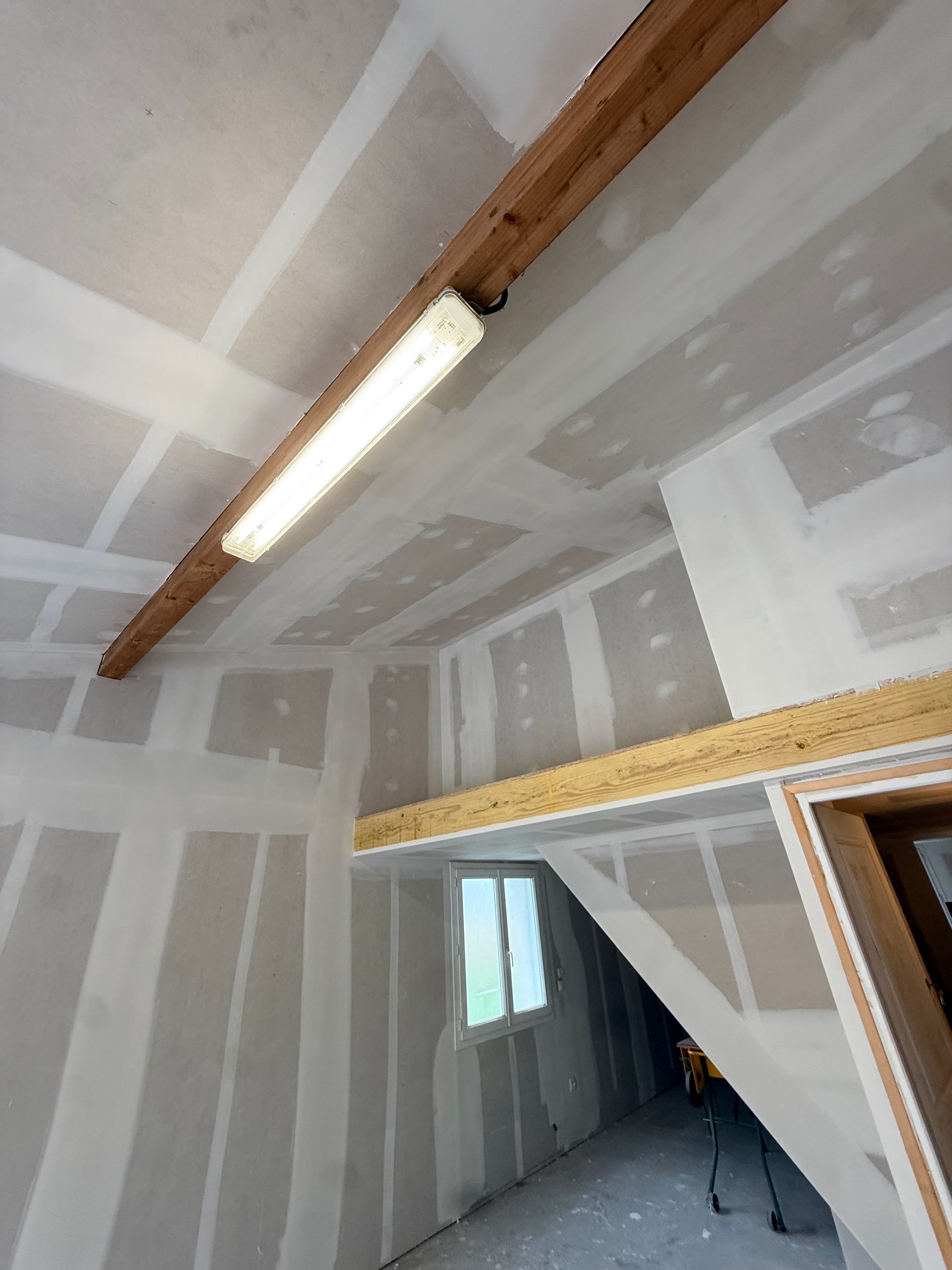 Pièce intérieure en cours de rénovation avec joints de cloisons sèches, poutre en bois apparente.