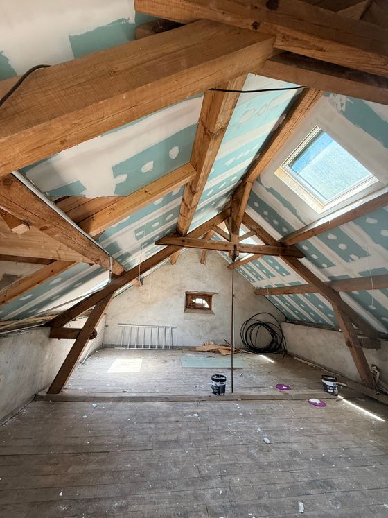 Intérieur du grenier avec poutres apparentes, panneaux d'isolation bleus et plancher en bois.