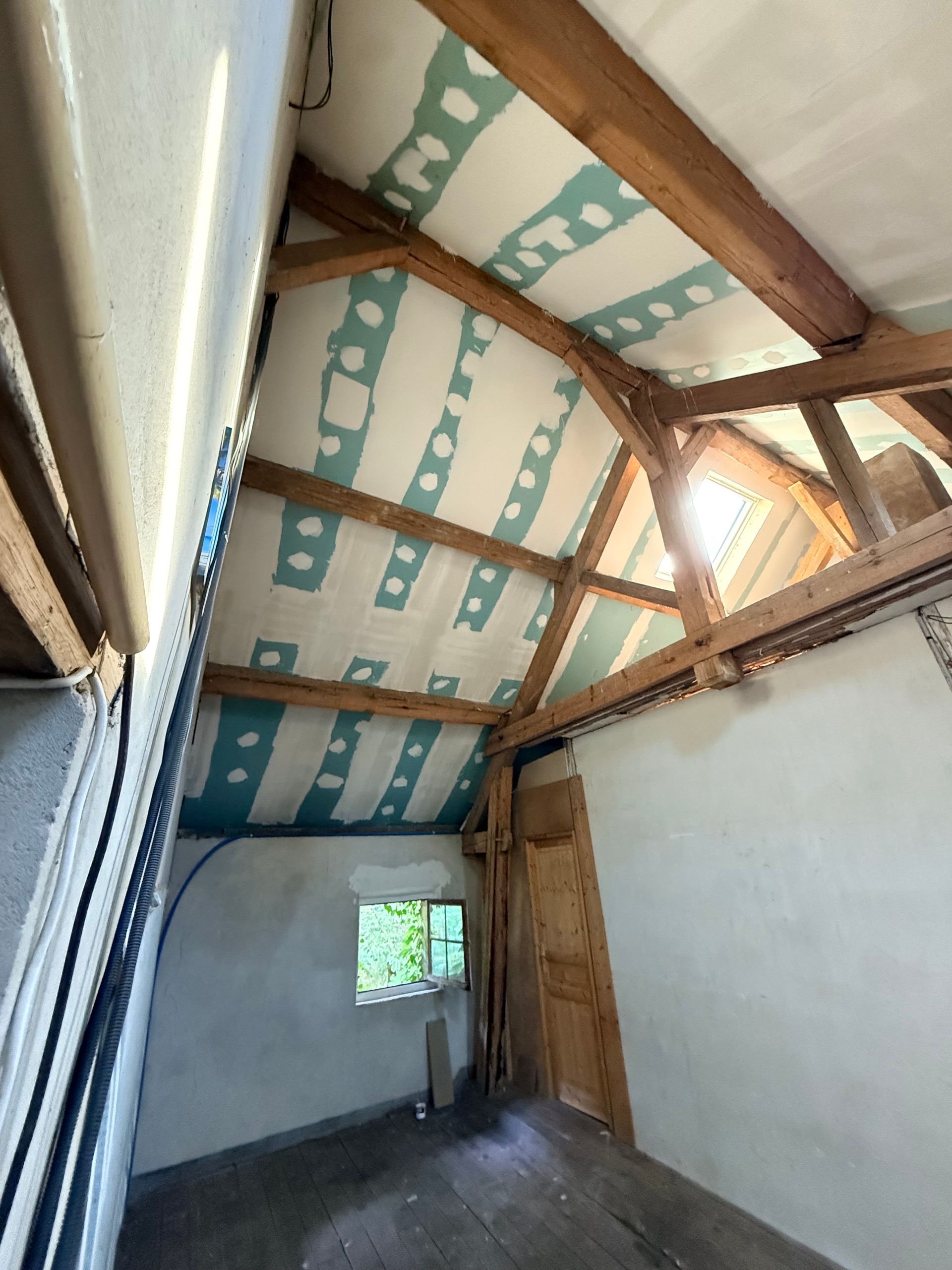 Intérieur d'une petite pièce avec poutres apparentes et toit en pente recouvert de panneaux isolants.