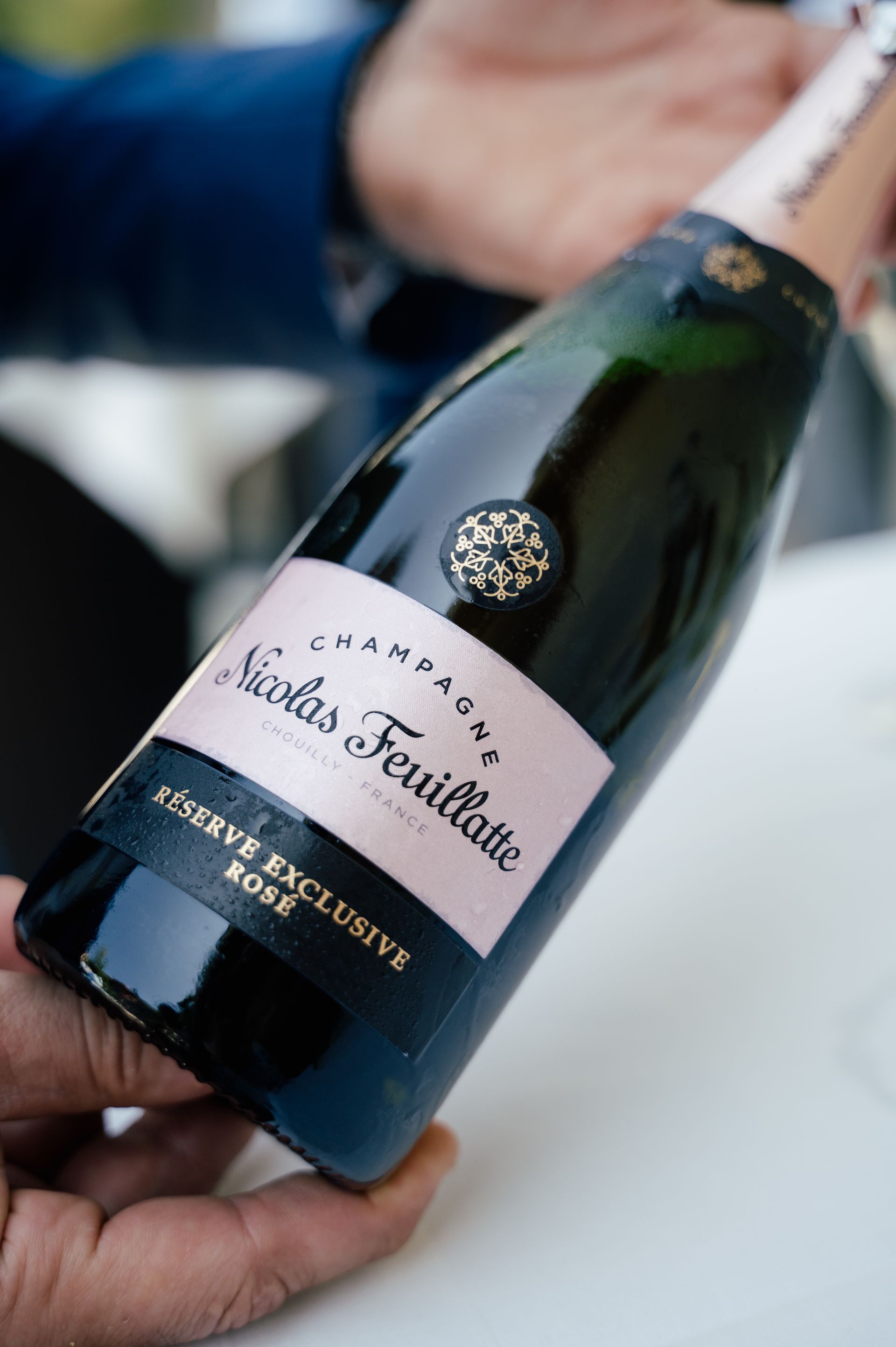 In einer Nahaufnahme hält eine Hand eine Flasche Nicolas Feuillatte Réserve Exclusive Rosé Champagner.
