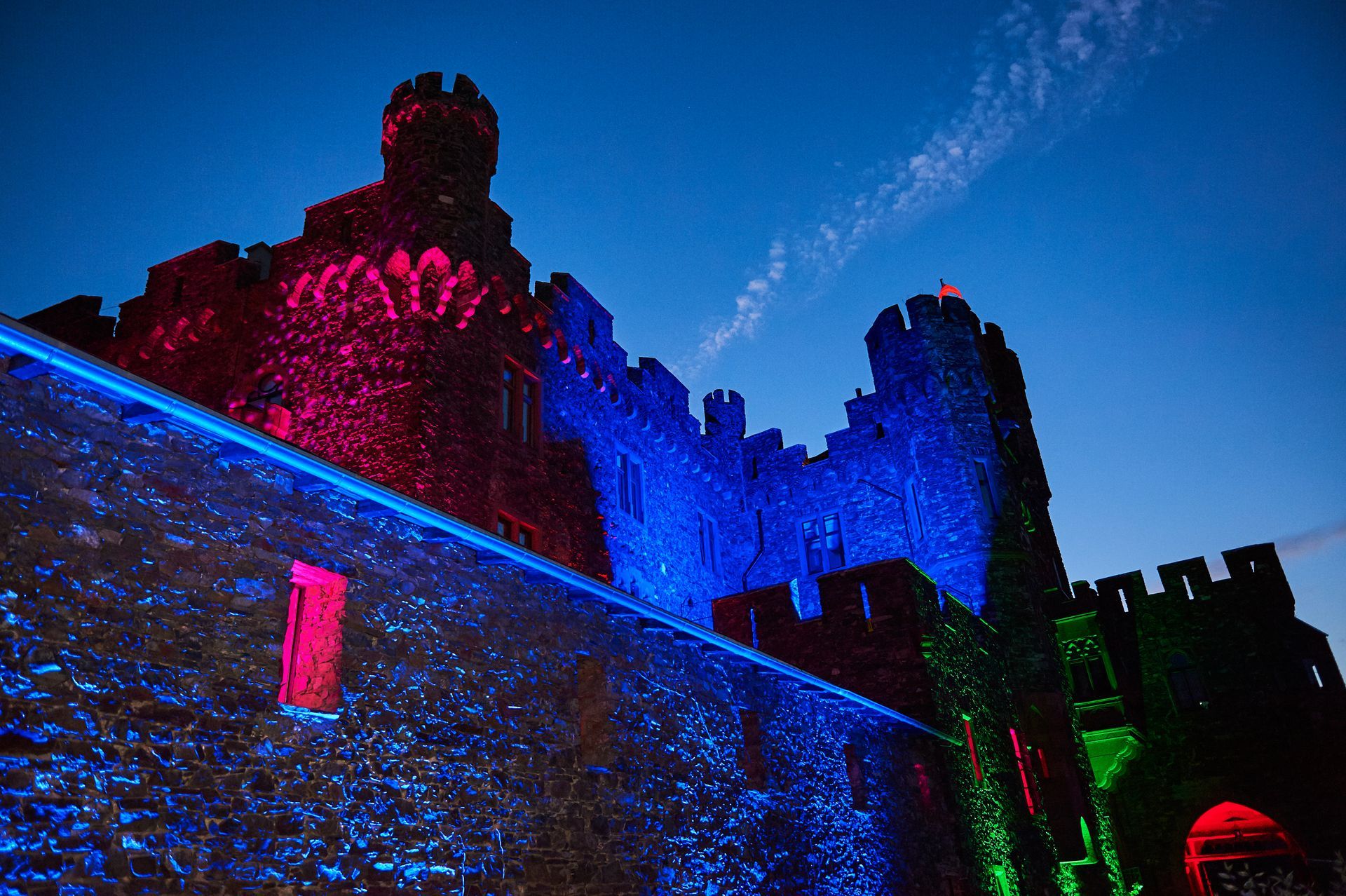 Eine steinerne Burg in der Abenddämmerung, deren Mauern von leuchtend roten, blauen und grünen Projektionen erhellt werden.