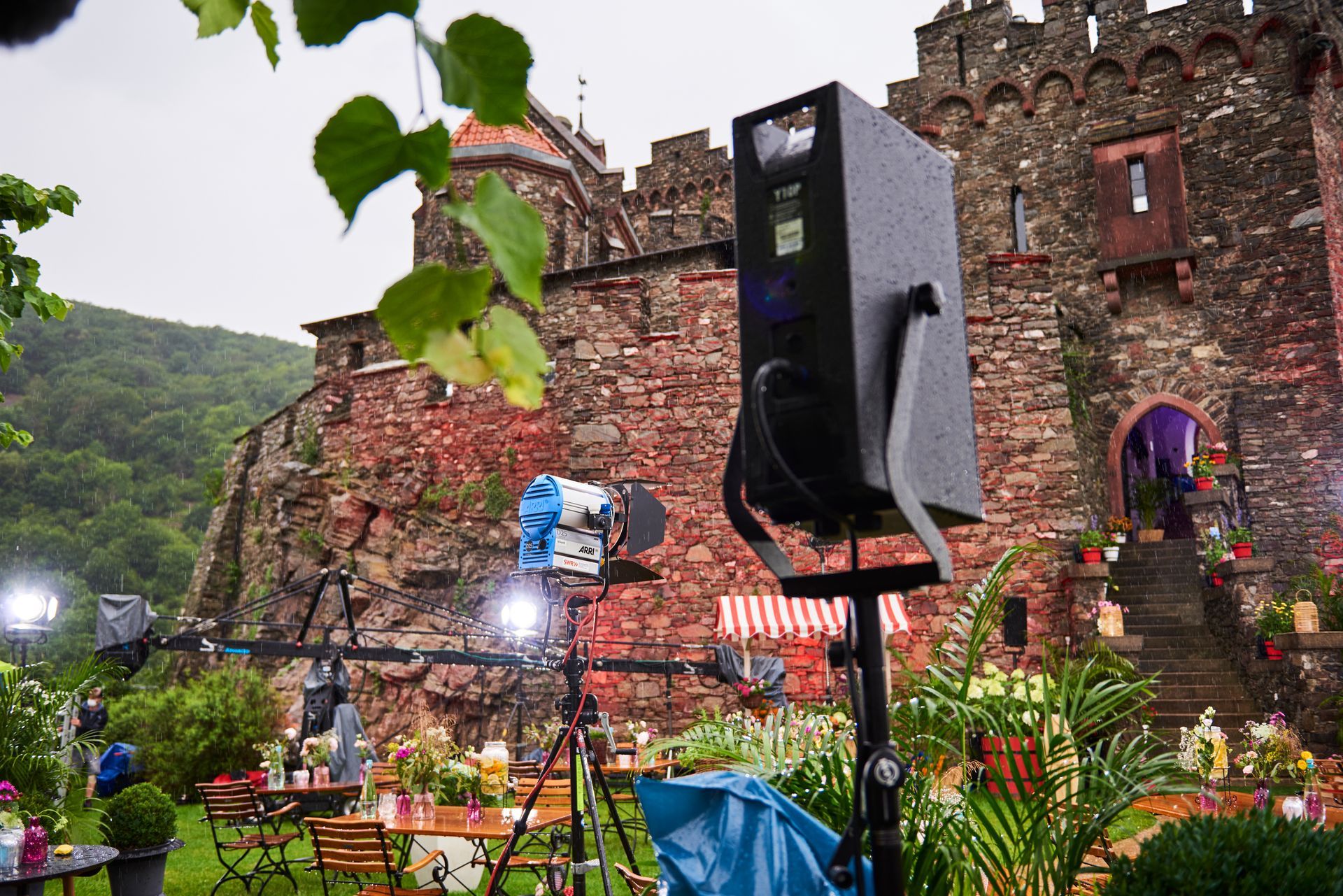 Professional film lighting equipment set up in a lush garden in front of a historic stone castle.