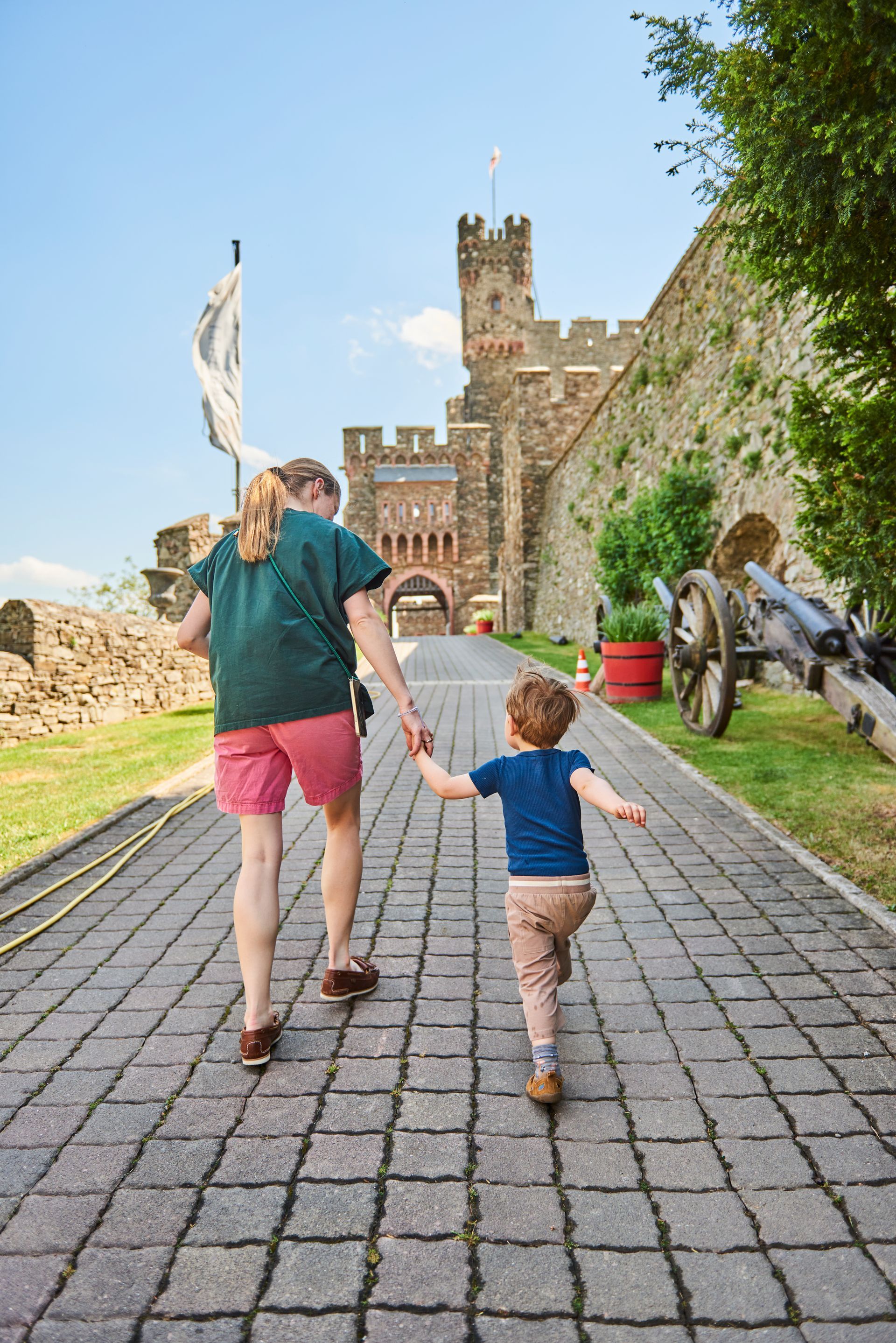 An adult and a child are walking hand in hand along a stone path toward the entrance to a historic castle.