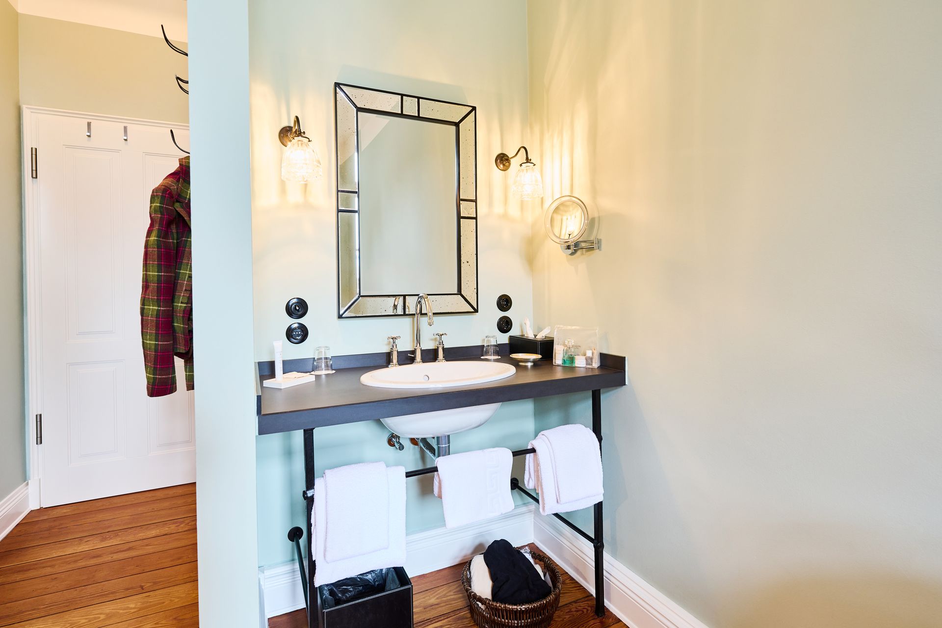 A bathroom cabinet with a white sink, a rectangular mirror, two wall sconces, and white towels hanging in a bright room.