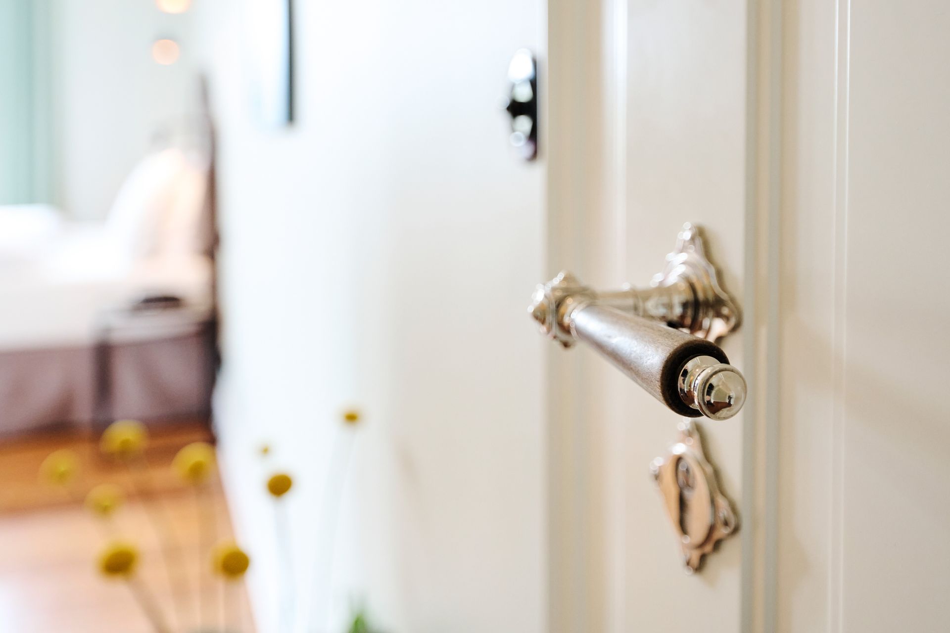 Ein silberner Türgriff und ein Schlüsselloch an einer weißen Innentür, im Hintergrund ist ein verschwommenes Schlafzimmer zu sehen.