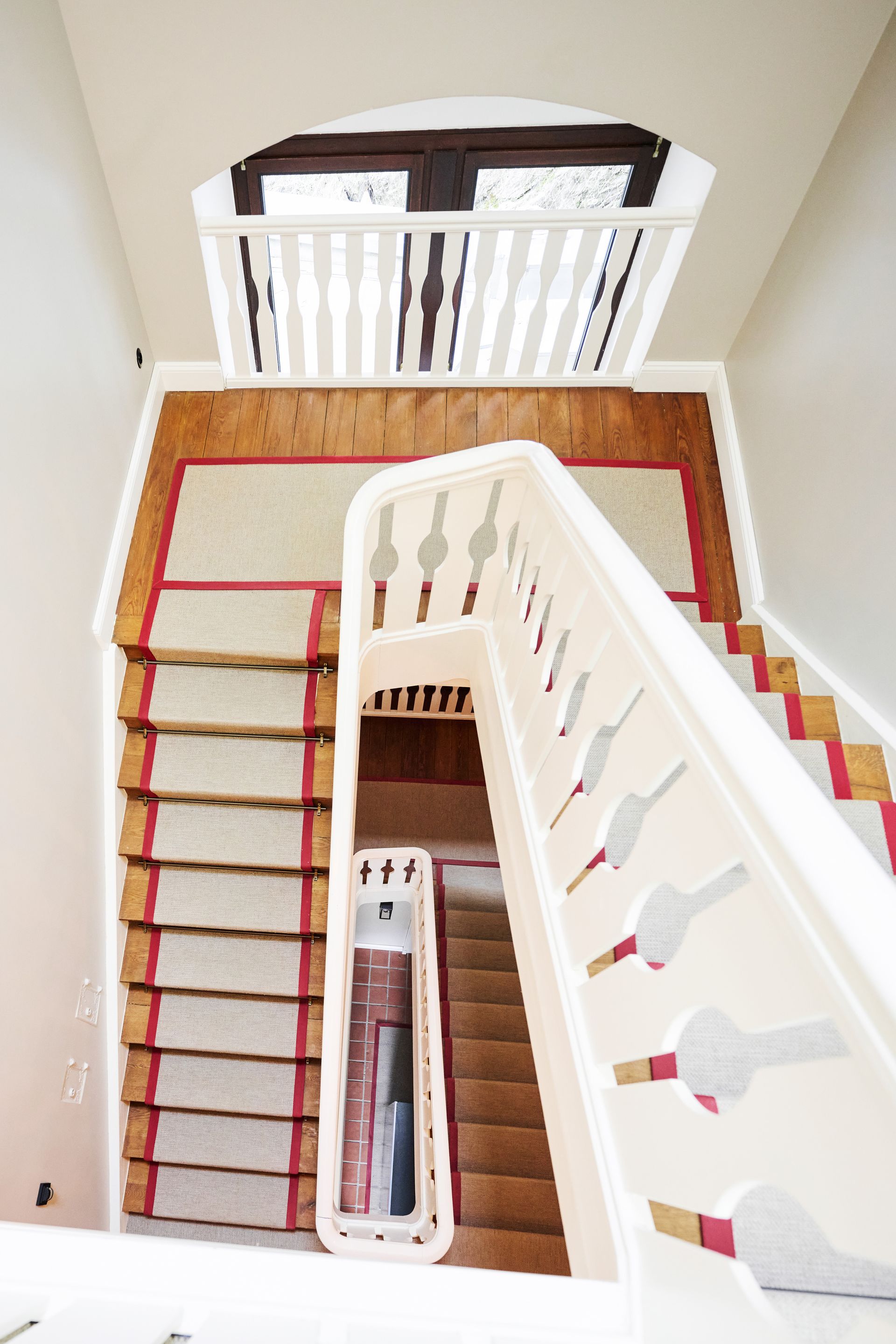 A staircase with a wooden railing and a light-colored rug with red stripes, viewed from above.