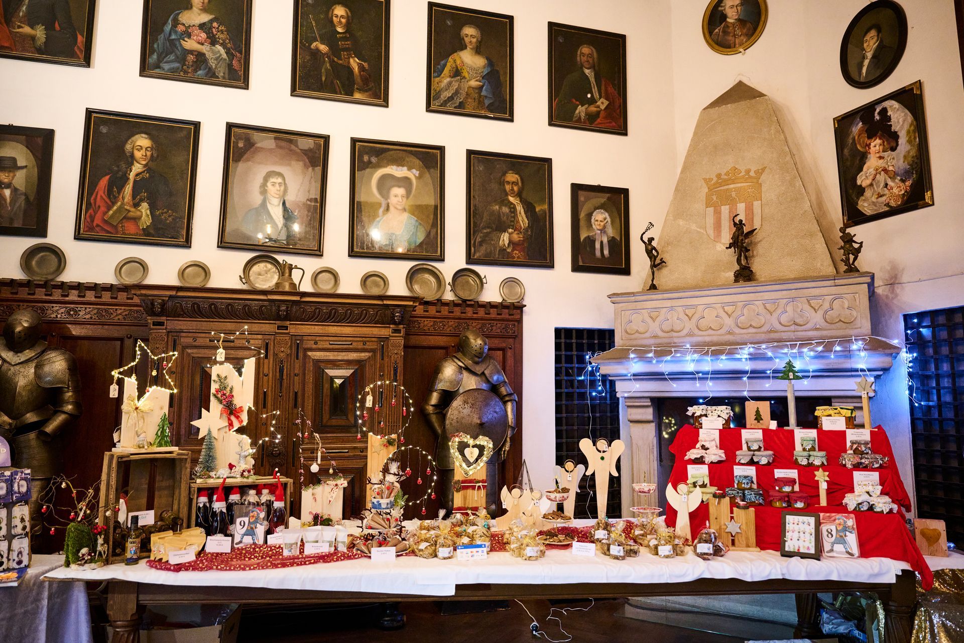 Ein Tisch mit verschiedenen Weihnachtsdekorationen in einem historischen Raum mit Porträts und Rüstungen an den Wänden.