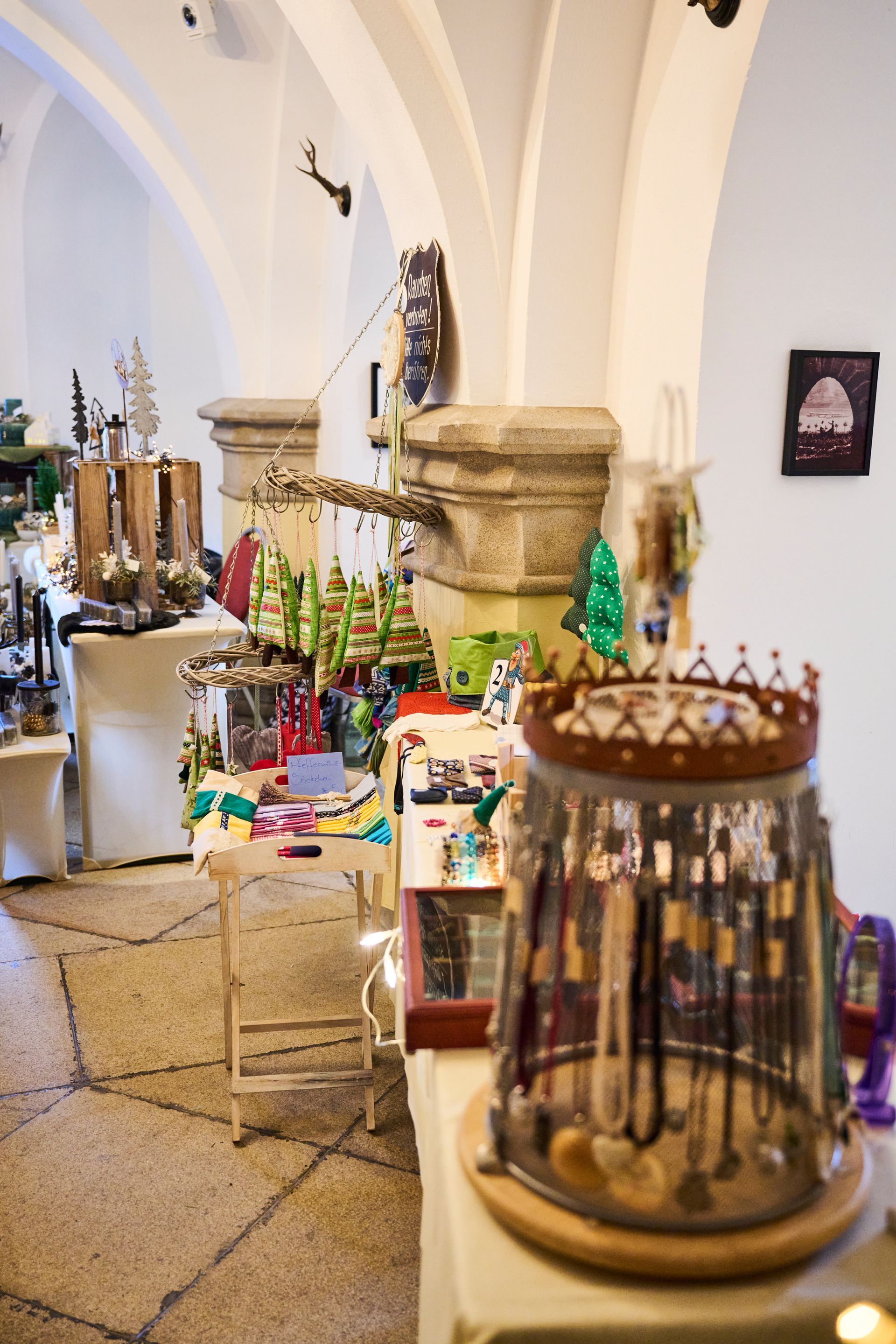 In einem mit Kunsthandwerk und Weihnachtsartikeln gefüllten, steingewölbten Raum steht auf einem Tisch eine dekorative Schmuckvitrine.