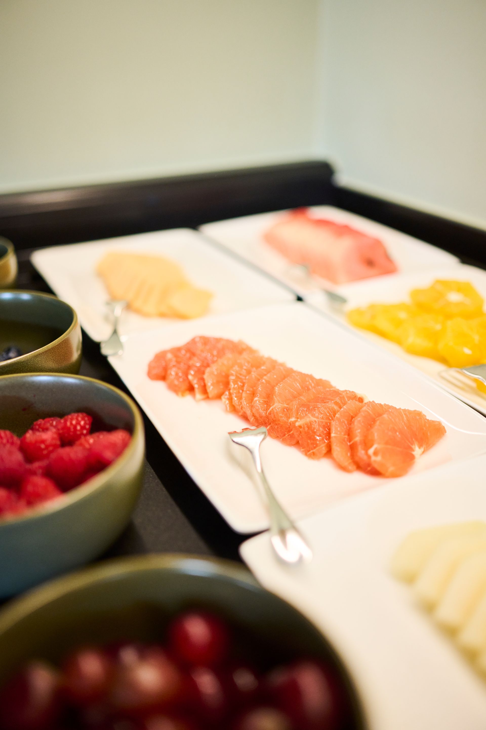 Ein Buffet mit Schüsseln voller Beeren und Kirschen sowie weißen Servierplatten mit geschnittenen Zitrusfrüchten und Melone.