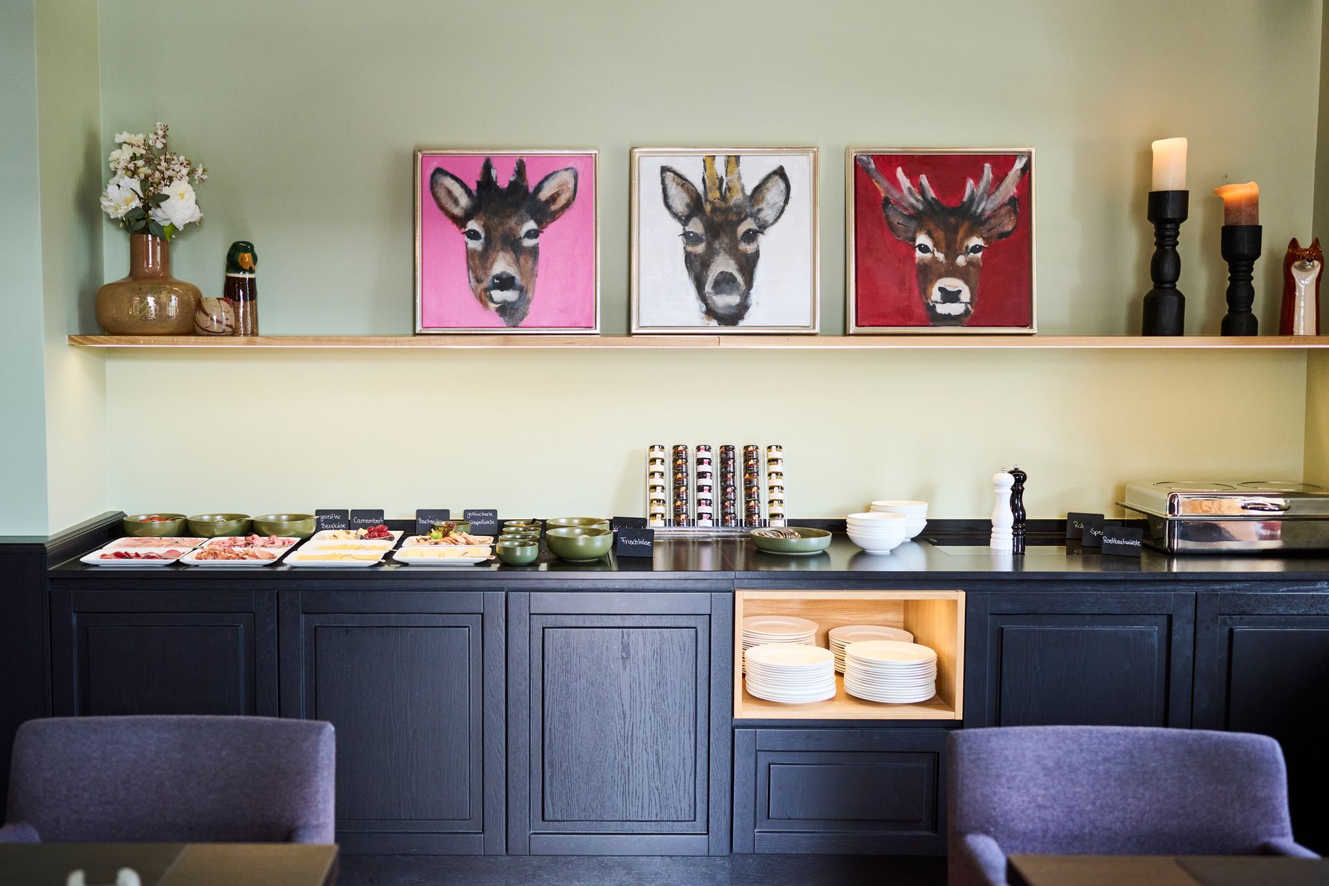 Ein Frühstücksbuffet mit Tabletts, Tellern und Tiermotiven auf einem Regal vor einer hellgrünen Wand.