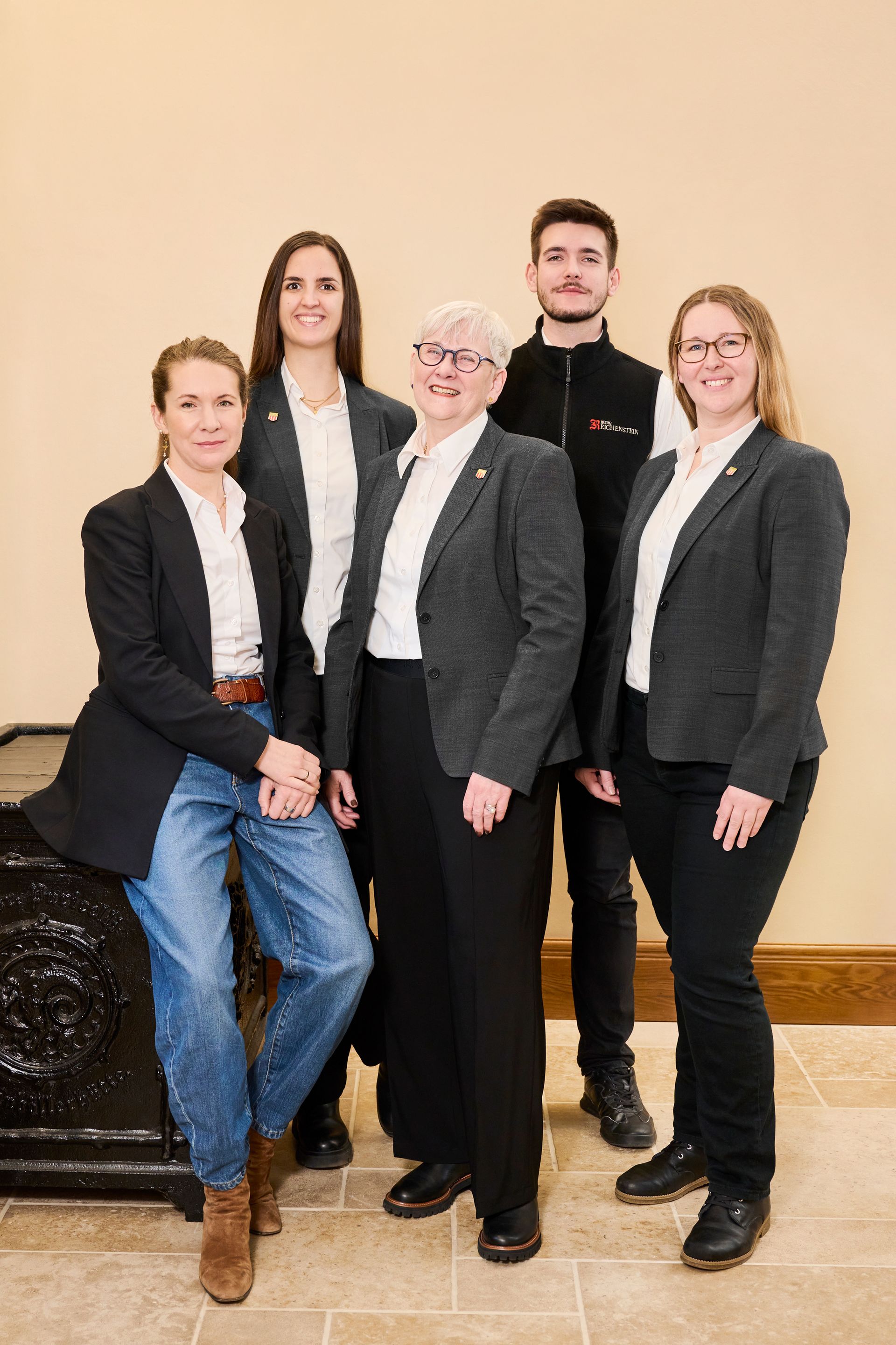 Eine Gruppe von fünf Personen in professioneller Geschäftskleidung, bestehend aus einheitlichen dunklen Blazern, steht zusammen in einem Innenraum.